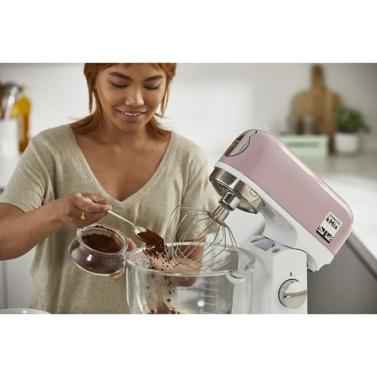 Una donna aggiunge cacao in polvere in un mixer a supporto Kenwood Kmix rosa.