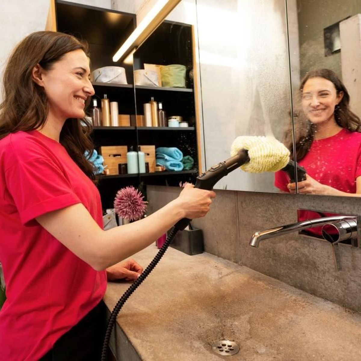 Una donna pulisce uno specchio del bagno con un pulitore a vapore.