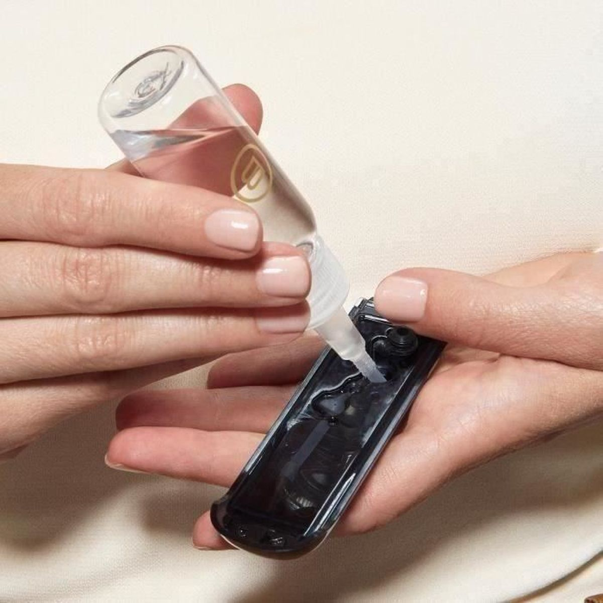 Dłonie wlewające płyn z butelki na czarne urządzenie, ujęcie z bliska.