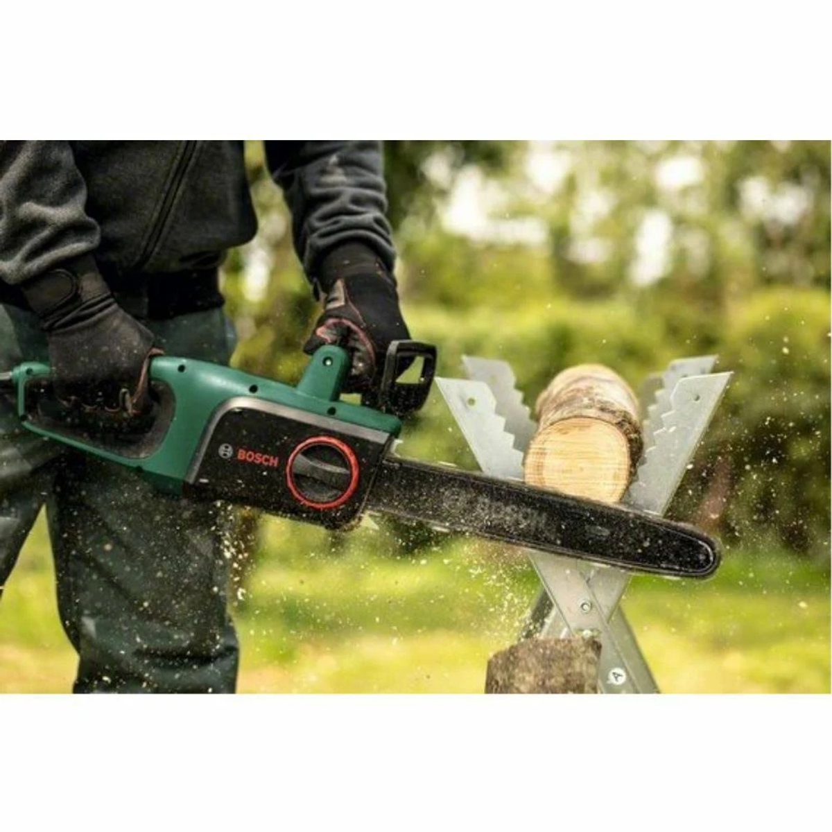 Osoba tnie kłodę zielono-czarną piłą łańcuchową na koziołku.