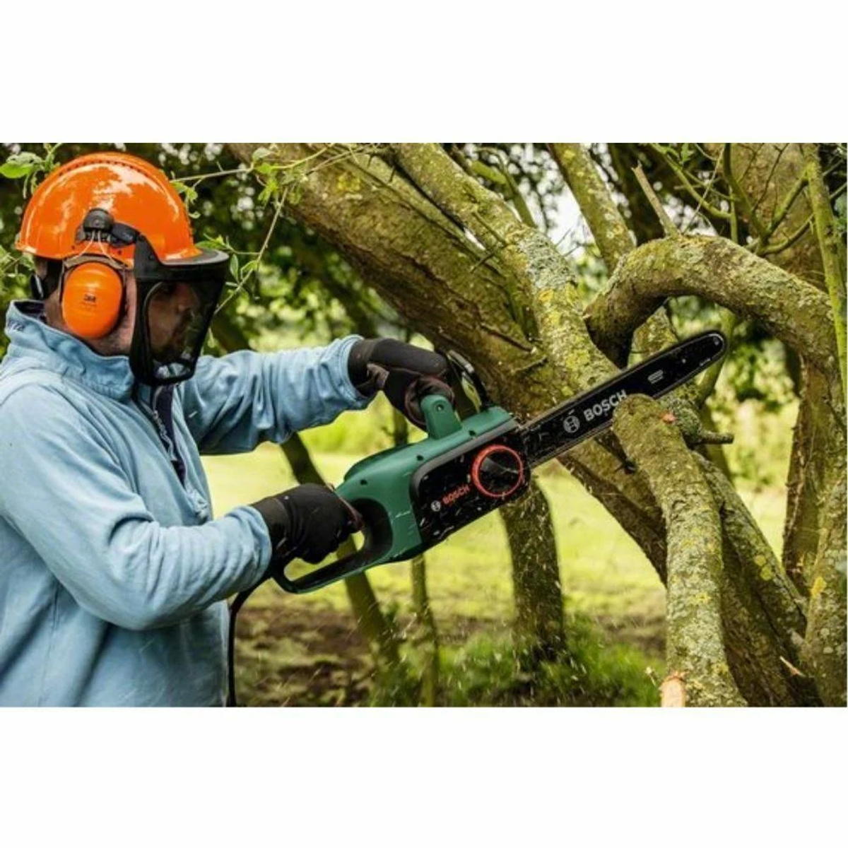 Mężczyzna używa zielono-czarnej piły łańcuchowej na gałęziach drzew, w sprzęcie ochronnym.