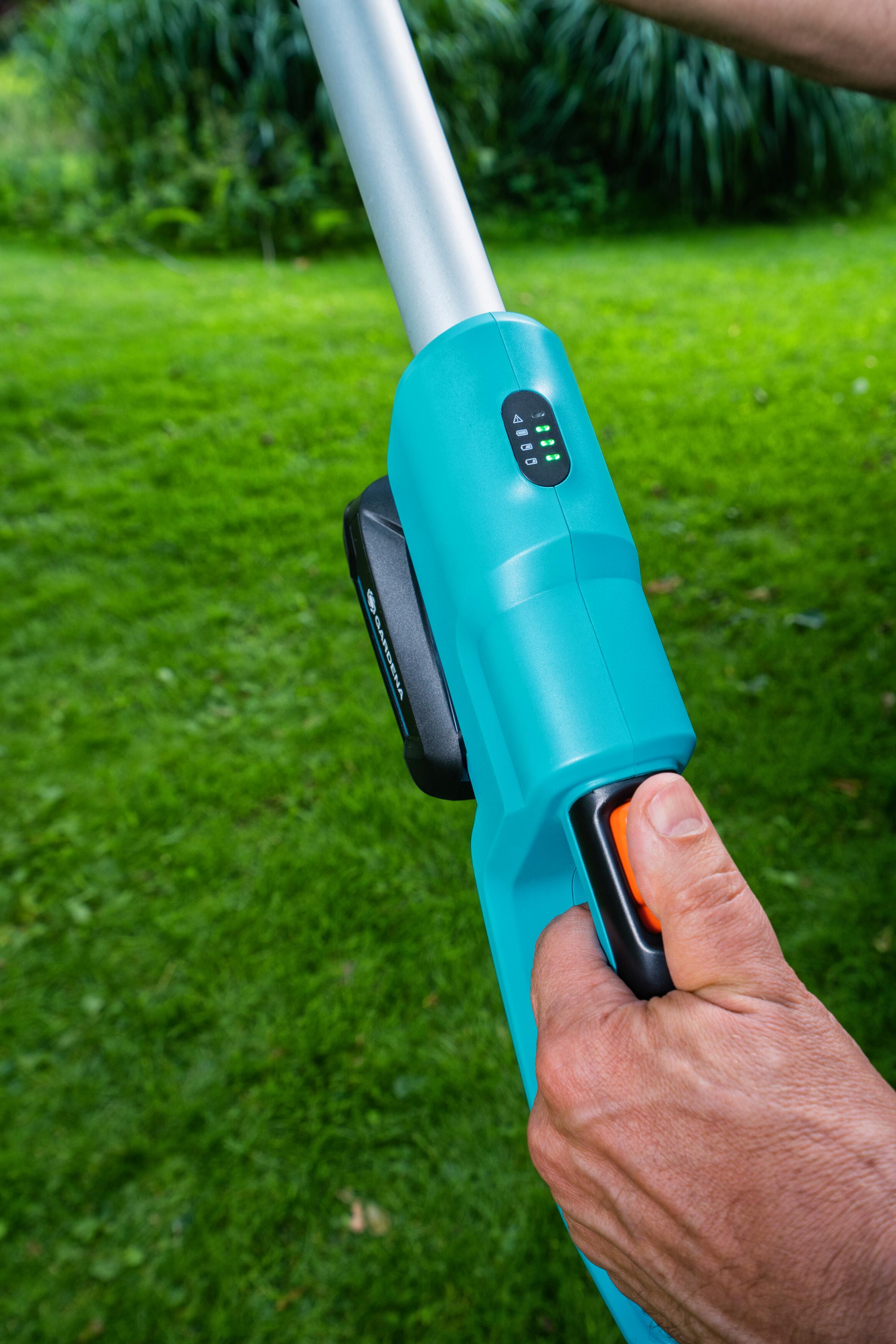 Una mano che tiene un attrezzo da giardinaggio turchese e nero con batteria.