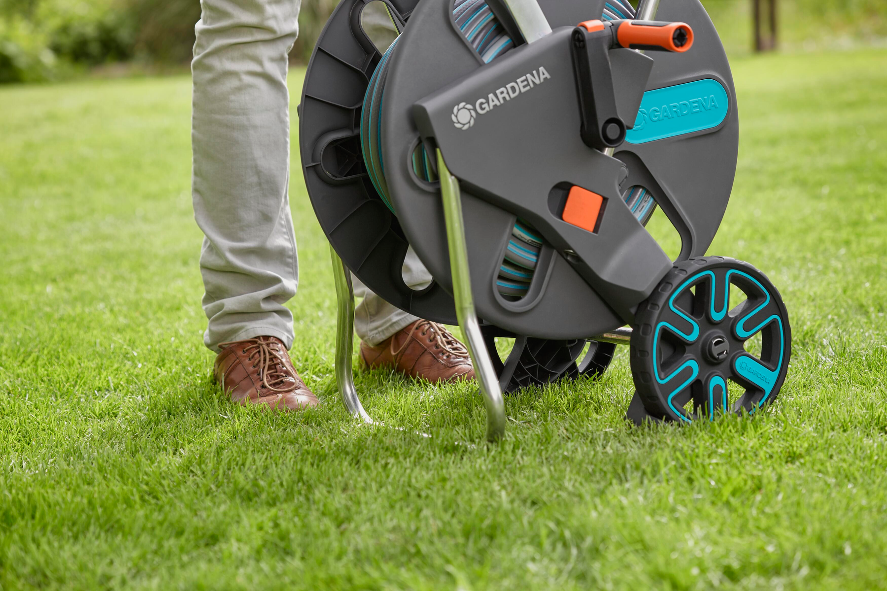 Person hält eine grüne Schlauchtrommel auf Gras. Schwarz-Türkis-Farben.