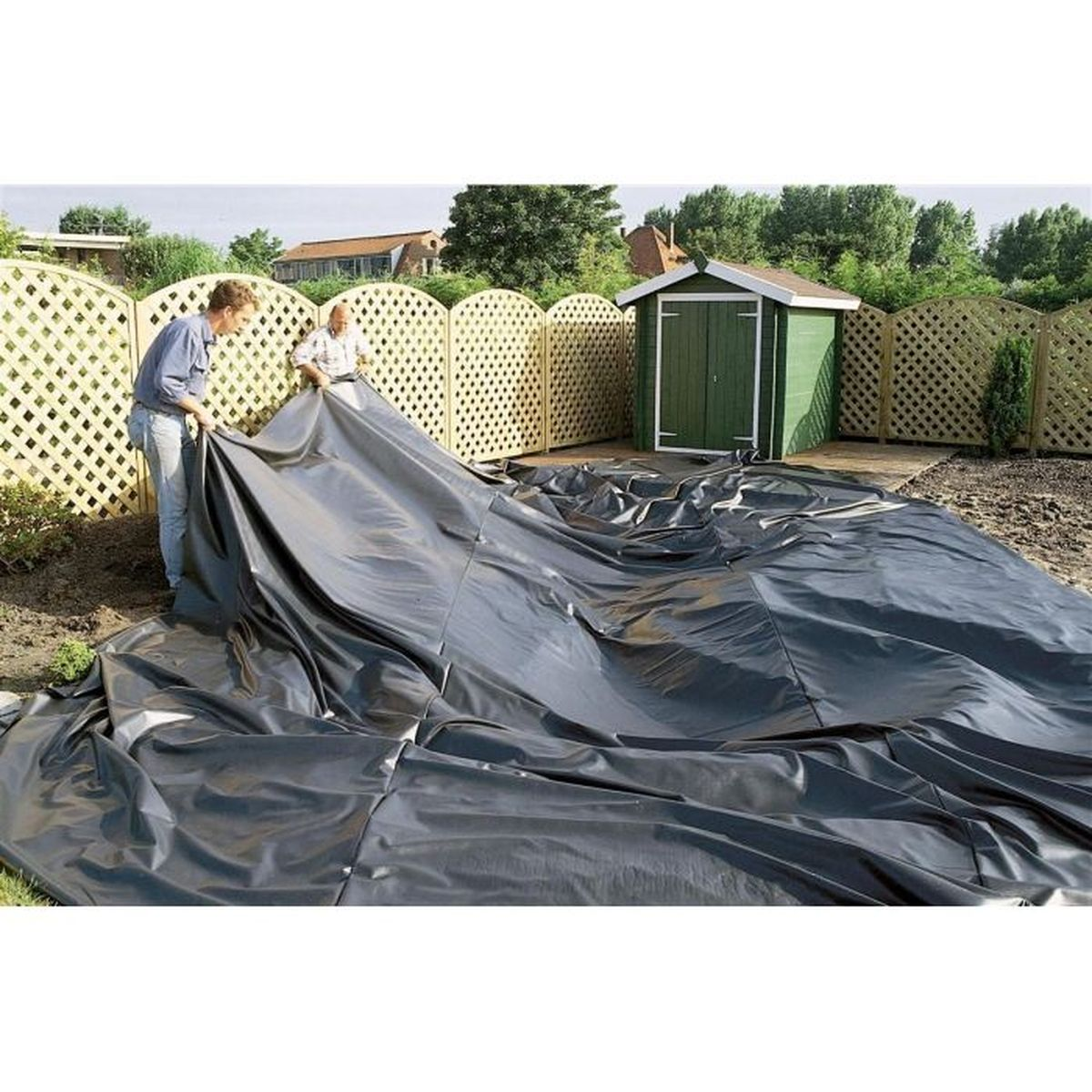 Zwei Personen legen eine große schwarze Plastikfolie auf ein Gartenbeet. Kleiner grüner Schuppen im Hintergrund.