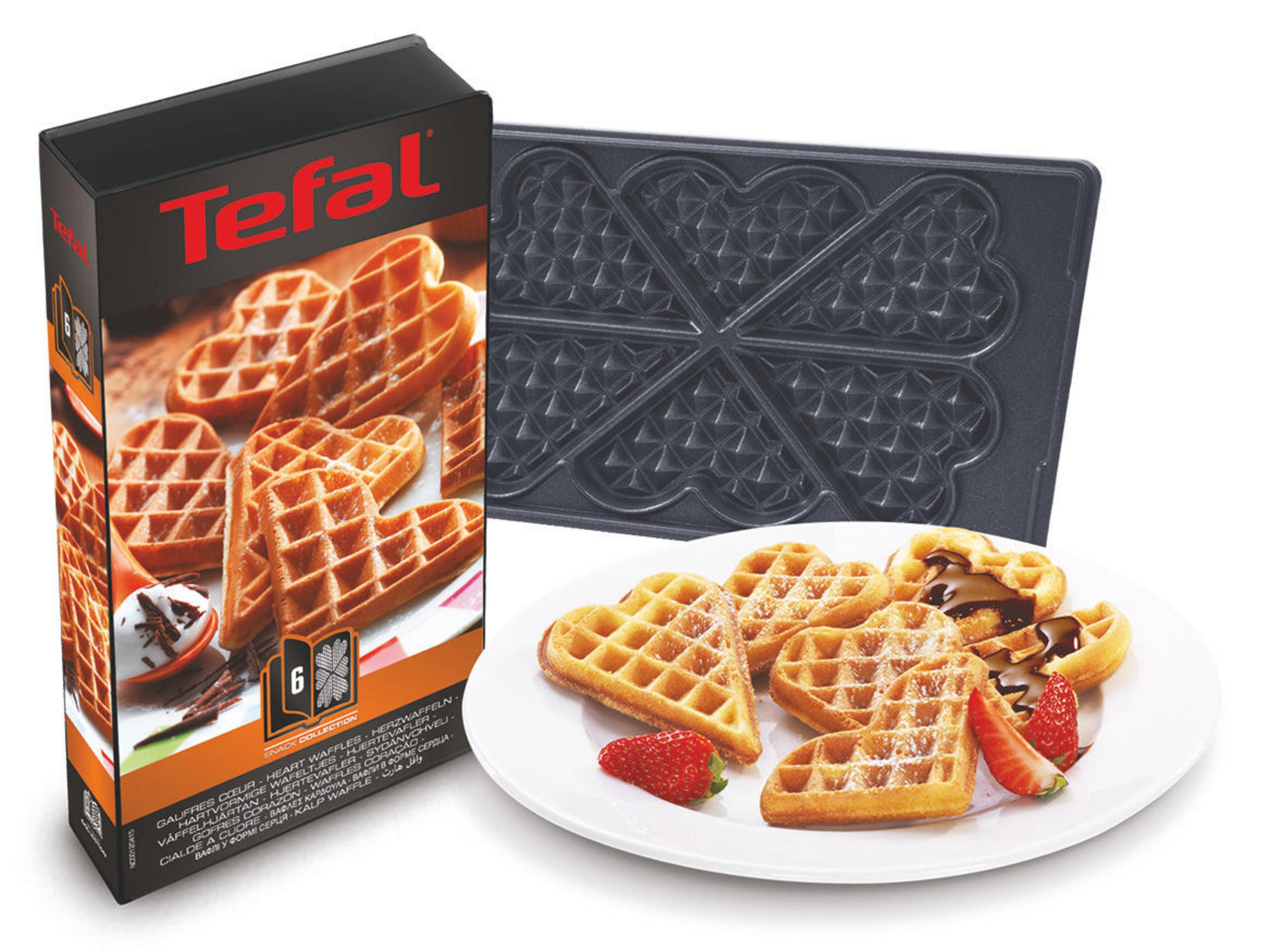 Tefal Waffeleisen in Herzform, Schachtel und Waffeln auf einem Teller mit Erdbeeren.