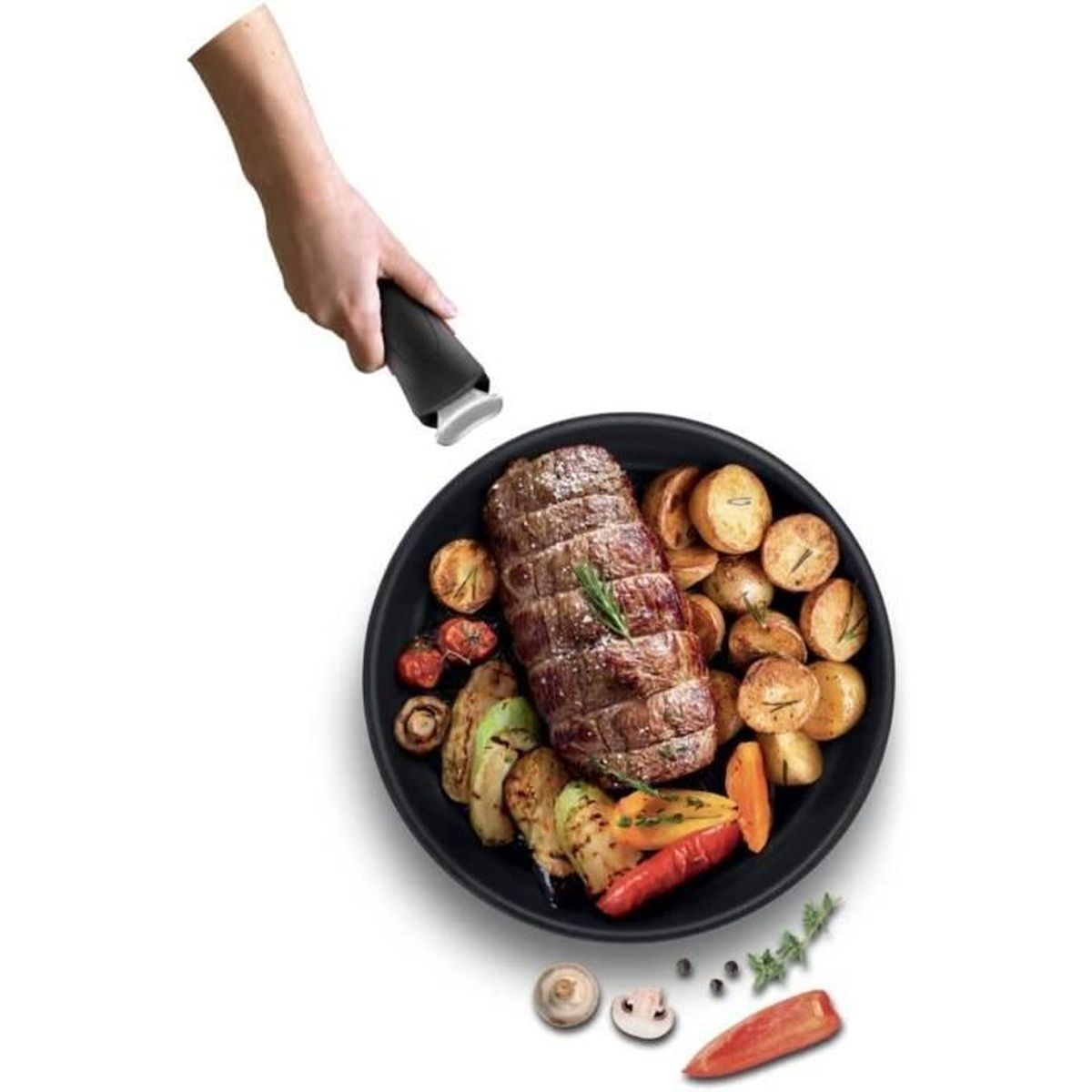 Gebratenes Fleisch und Gemüse auf schwarzem Teller, Hand hält Pfannengriff.
