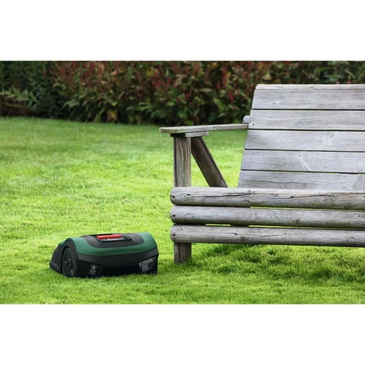 Ein Rasenroboter auf grünem Gras neben einer Holzbank. Der Mäher ist schwarz und grün.
