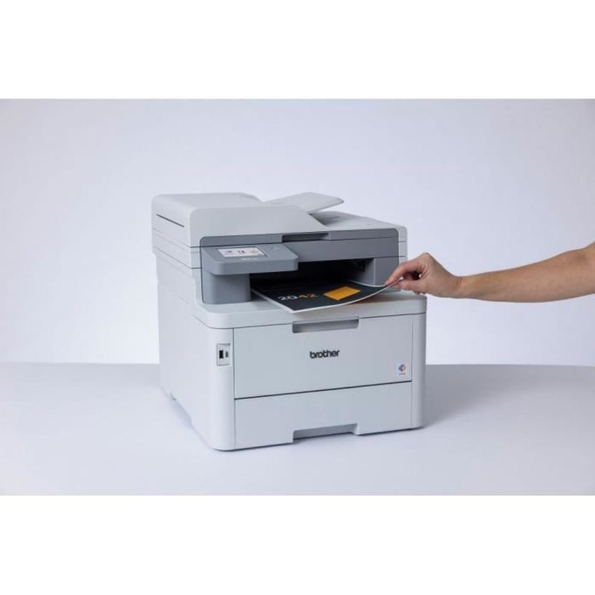 Persoon die een document in een witte printer steekt. De printer staat op een wit oppervlak.