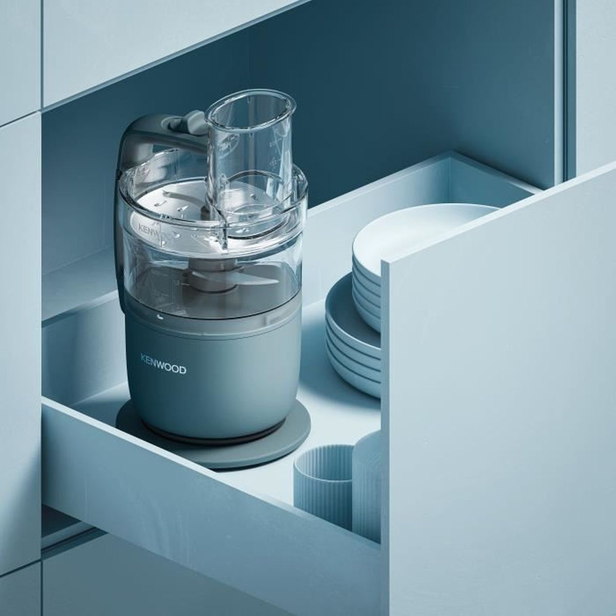 Un robot da cucina Kenwood grigio è in un cassetto accanto a piatti e tazze.