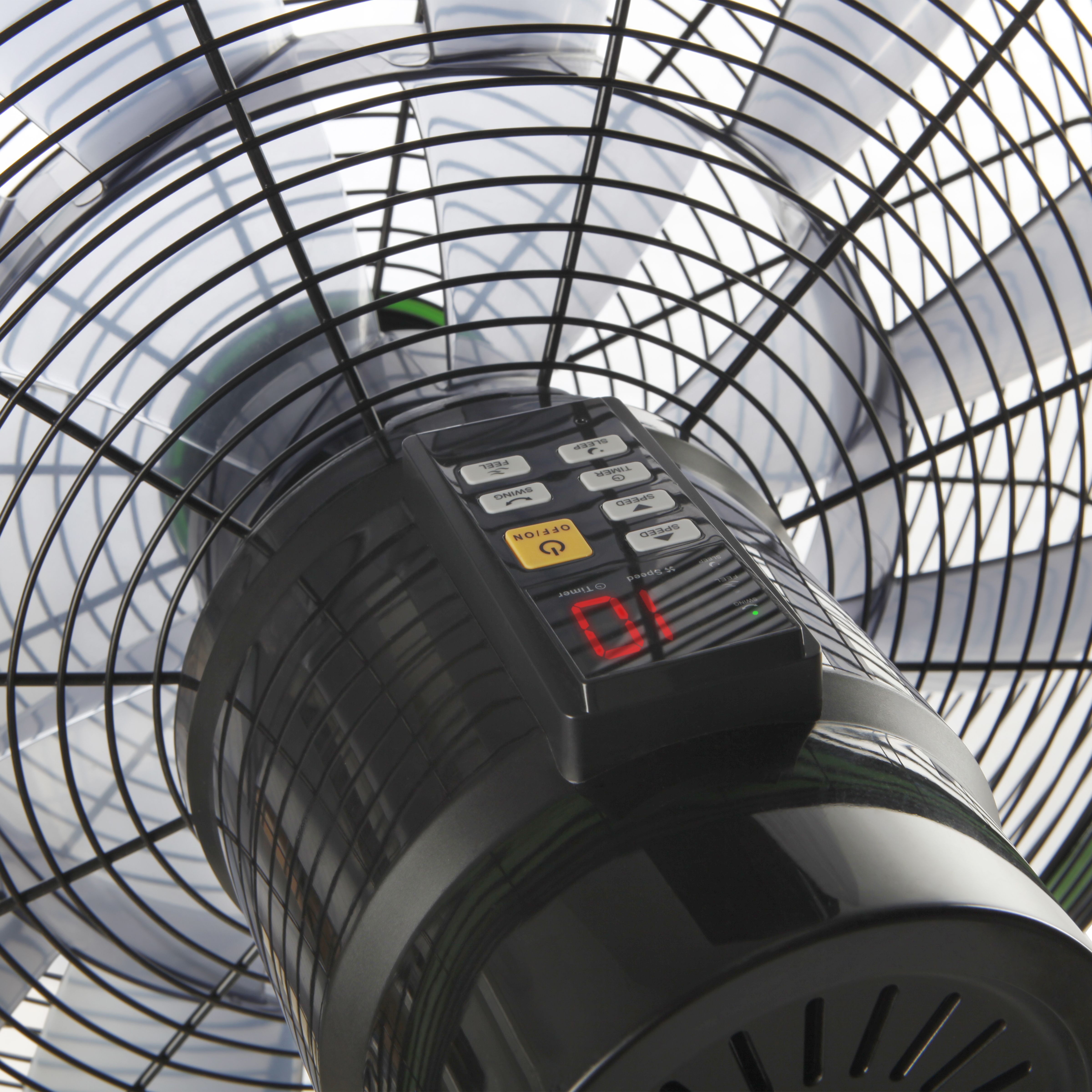 Zbliżenie czarnego wentylatora z pilotem. Wentylator ma drucianą klatkę i łopaty. Pilot ma wyświetlacz cyfrowy.