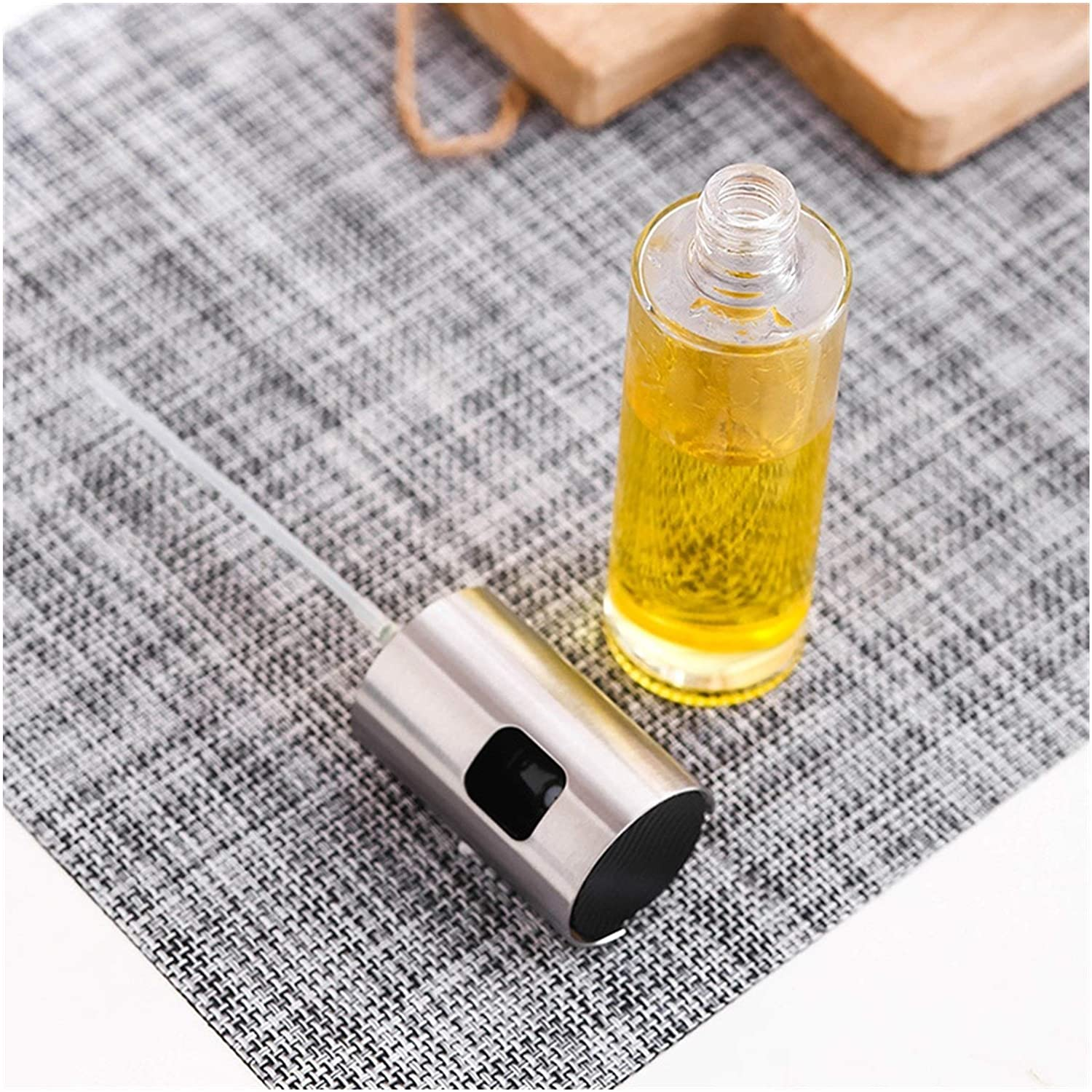 Butelka z rozpylaczem oleju z olejem w środku, obok stalowej dyszy na szarej powierzchni.