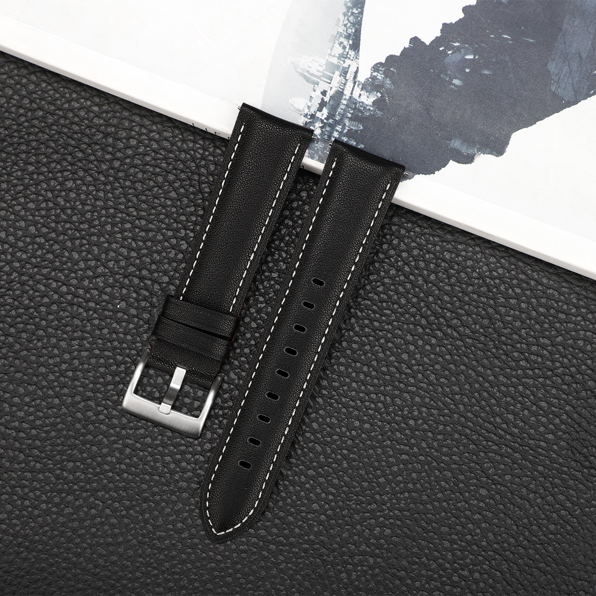 Dwa czarne skórzane paski do zegarków z białymi przeszyciami. Jest metalowa klamra.