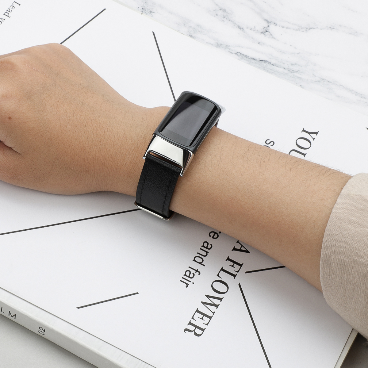 Czarny smartwatch z czarnym skórzanym paskiem i srebrną klamrą, na białym papierze.