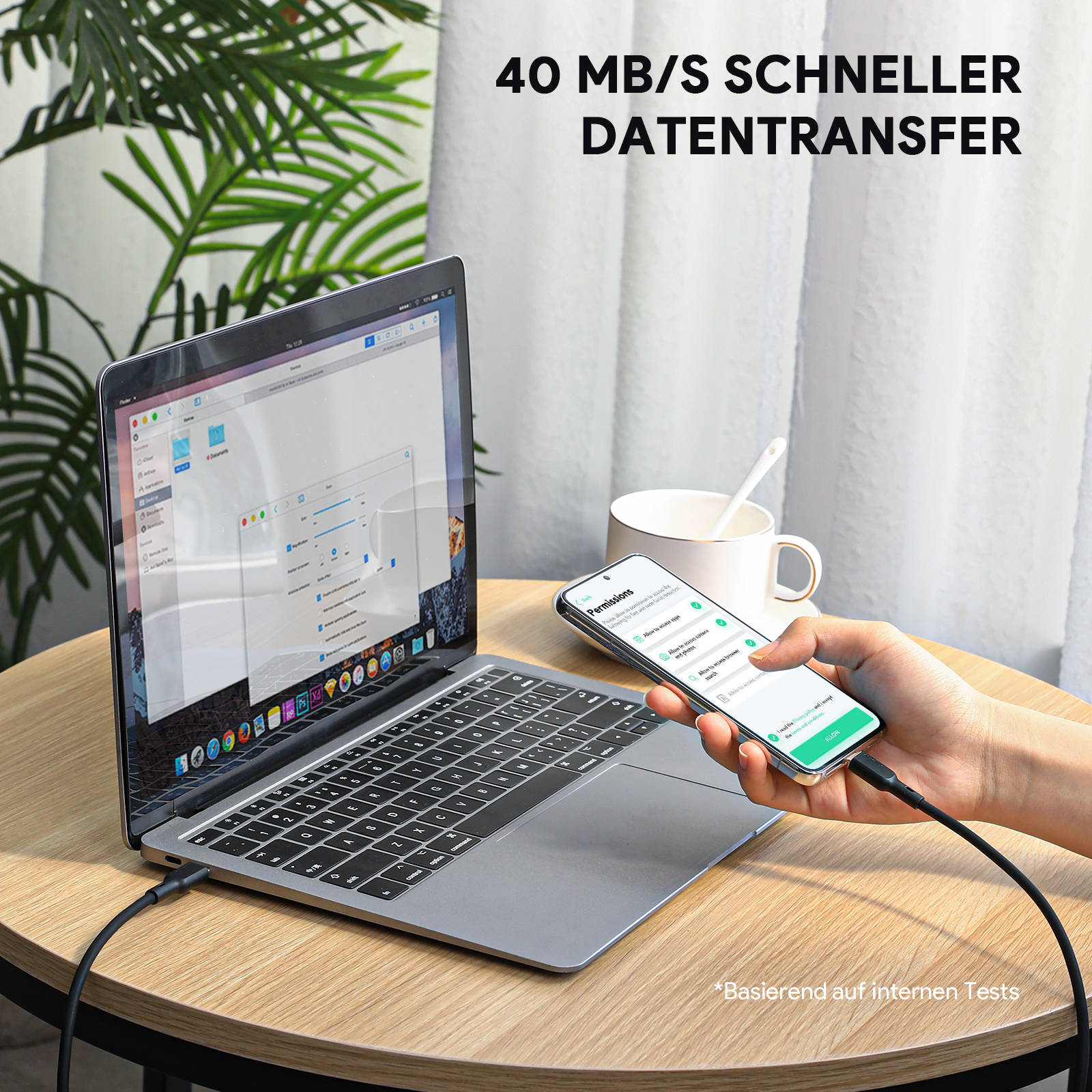 Person hält ein Telefon mit einem schwarzen Ladekabel, das mit einem Laptop verbunden ist.