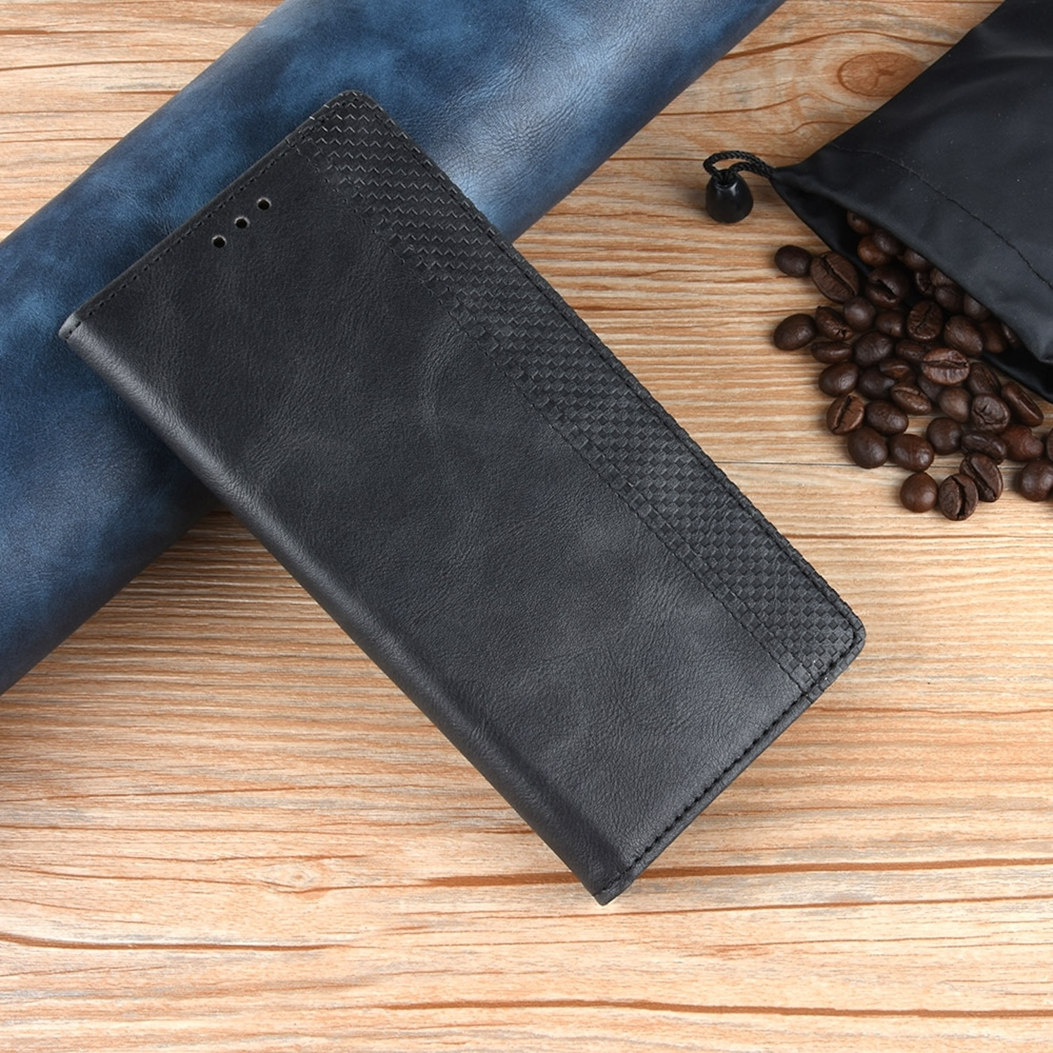 Schwarze Leder-Handyhülle mit strukturiertem Muster, geöffnet auf Holz, mit Bohnen und blauer Rolle.