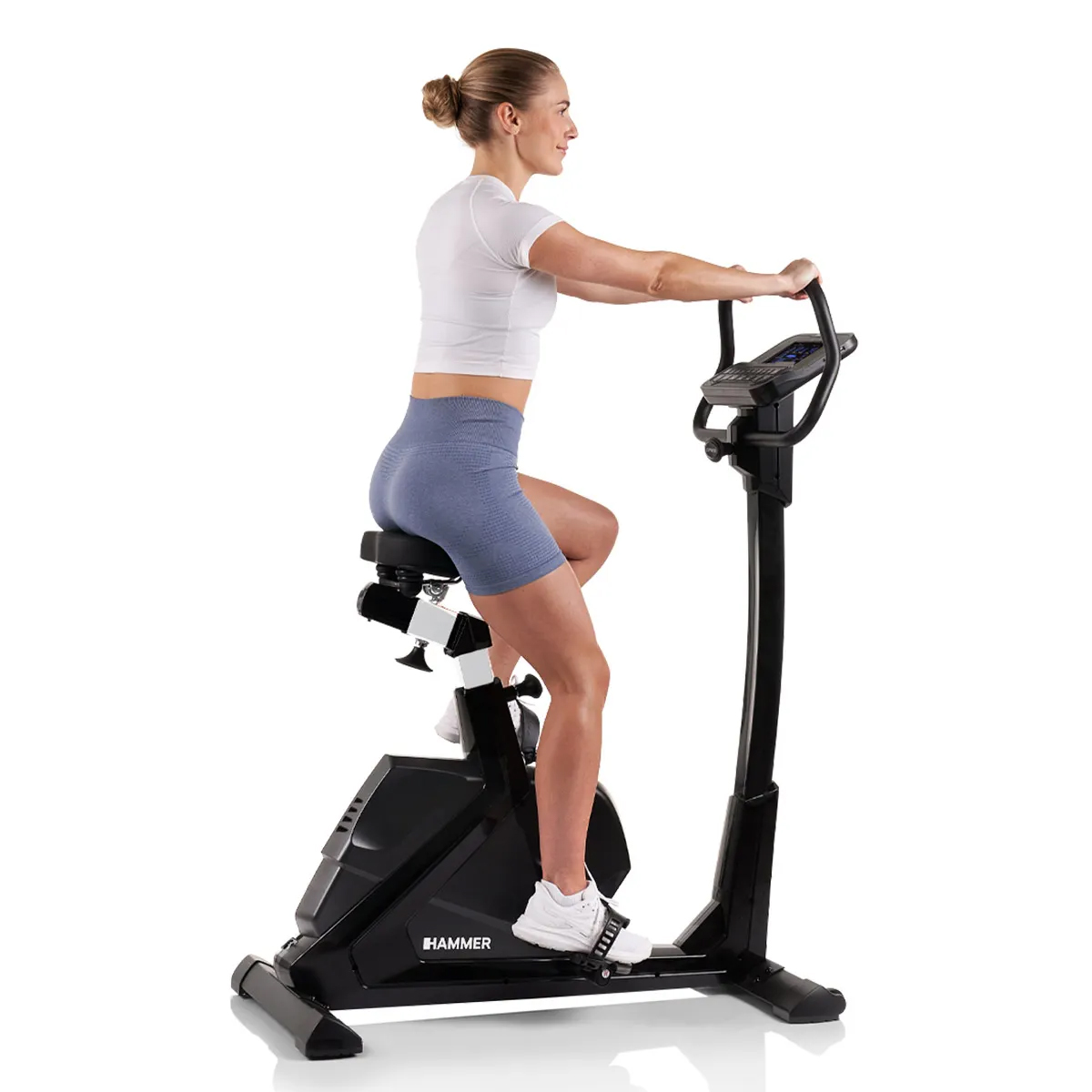 Eine Frau in Sportkleidung fährt drinnen auf einem stationären Heimtrainer, weißer Hintergrund.