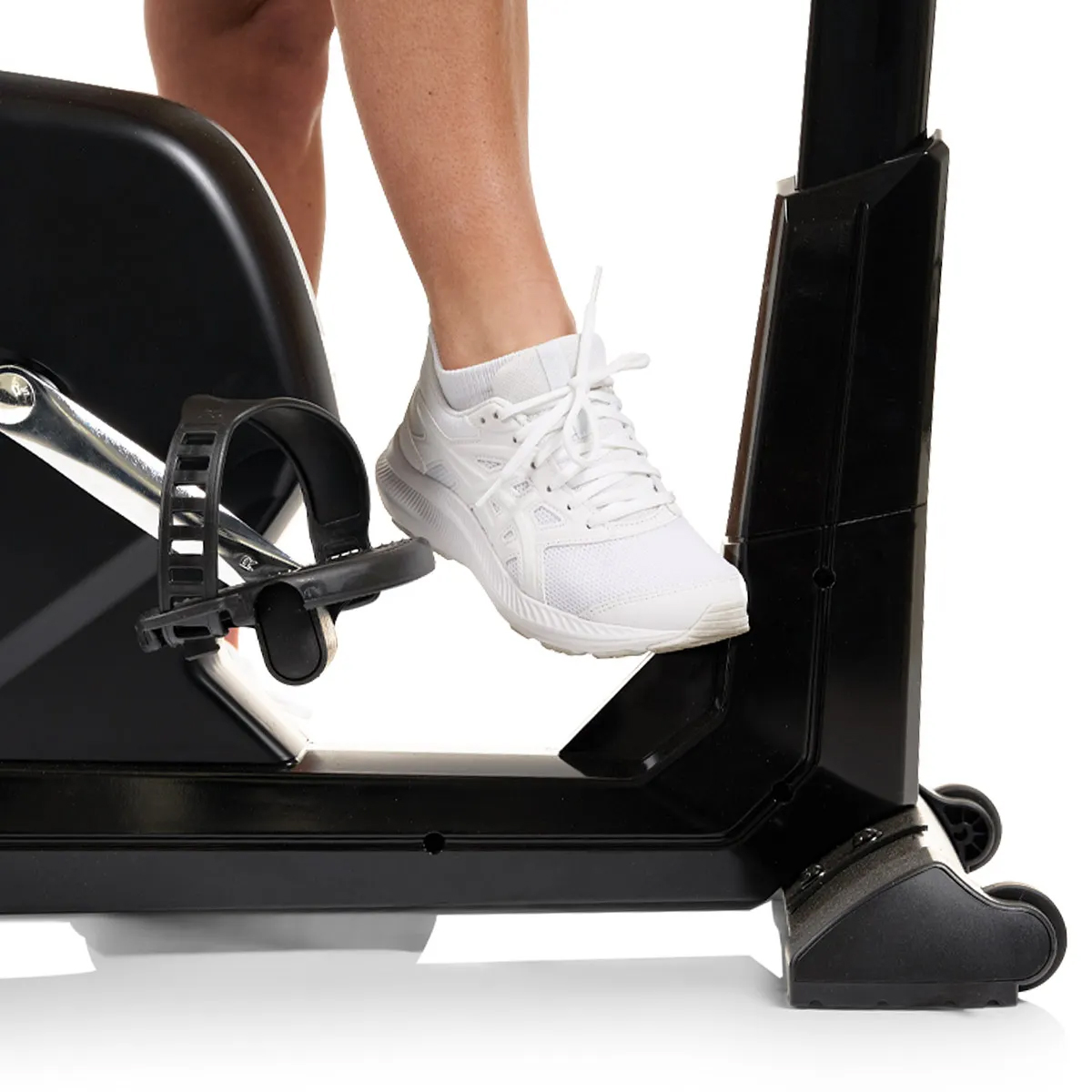 Der Fuß einer Person in einem weißen Turnschuh auf einem Pedal eines Heimtrainers.