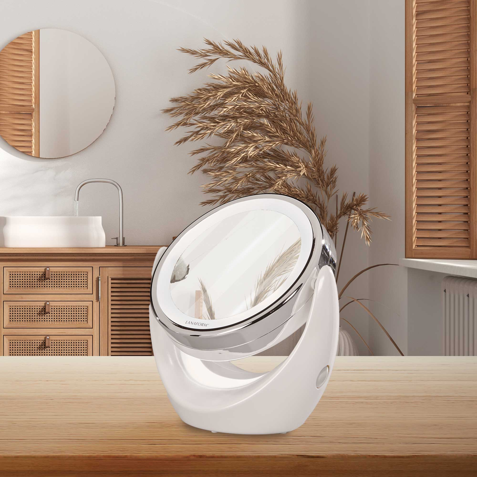 Ein weißer, oval geformter Schminkspiegel auf einem Holztisch. Ein Badezimmer mit Spiegel und Pflanze im Hintergrund.