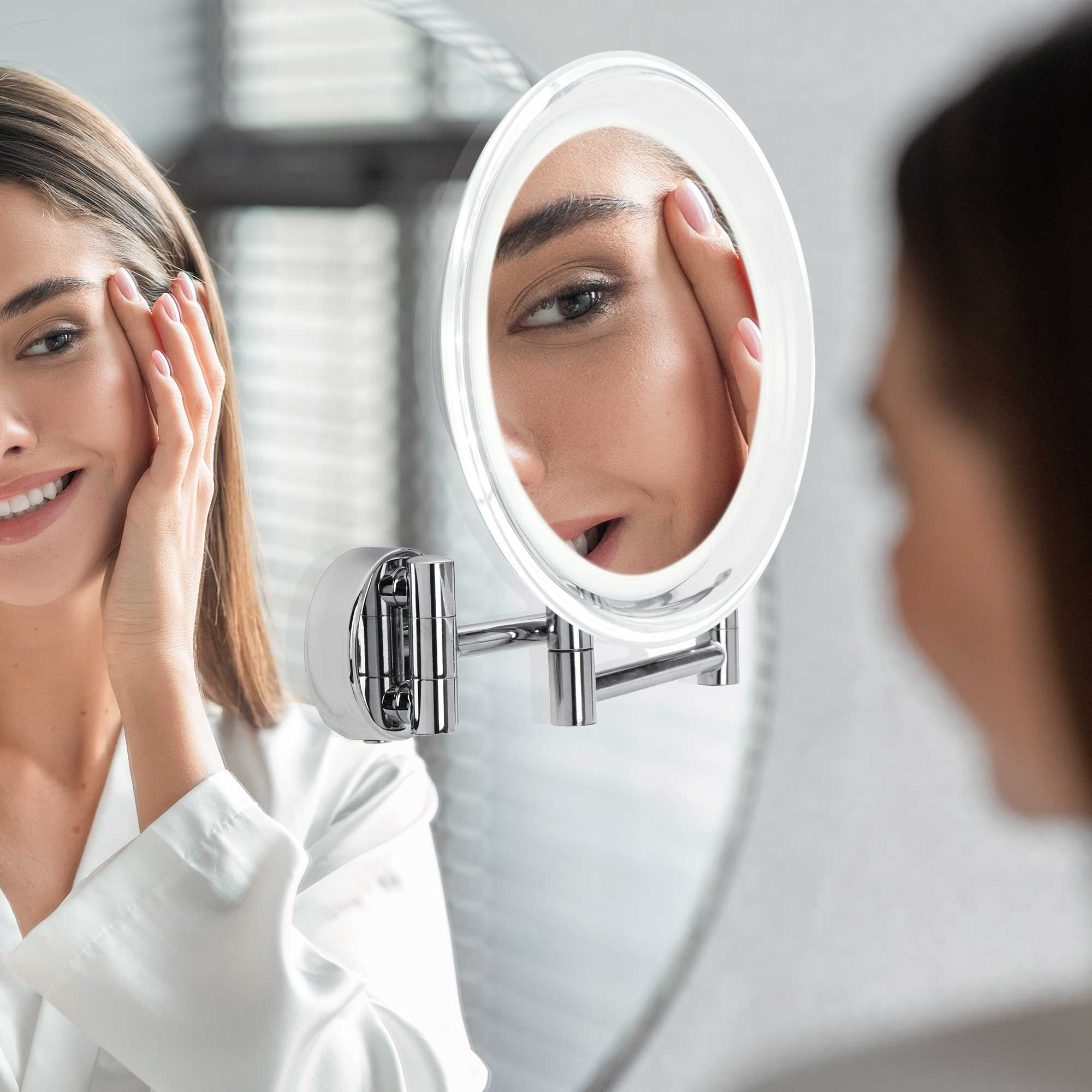 Frau betrachtet ihr Gesicht in einem beleuchteten Spiegel, mit einem anderen Spiegel, der ihr Bild reflektiert.