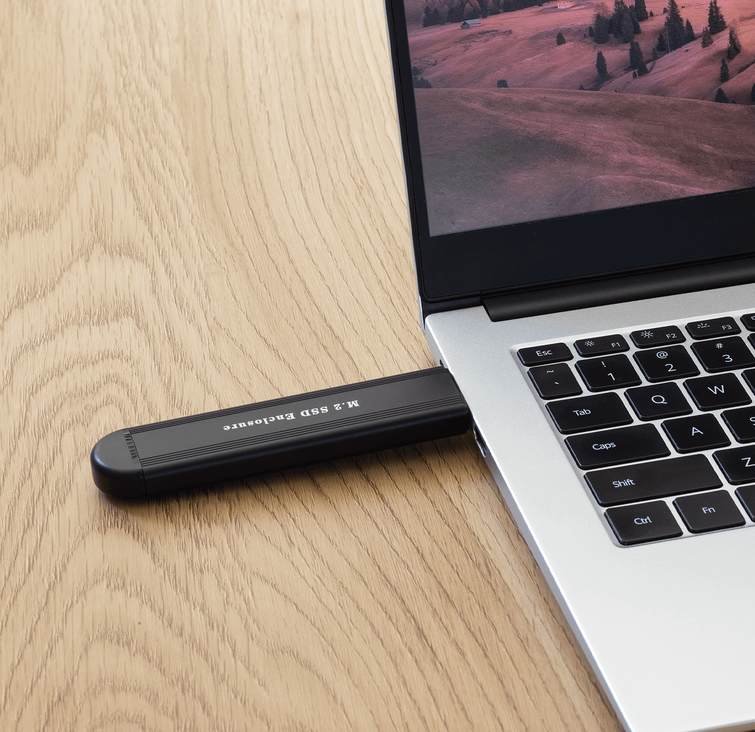 Schwarzes M.2 SSD-Gehäuse, das an einem Laptop auf einem Holztisch angeschlossen ist.