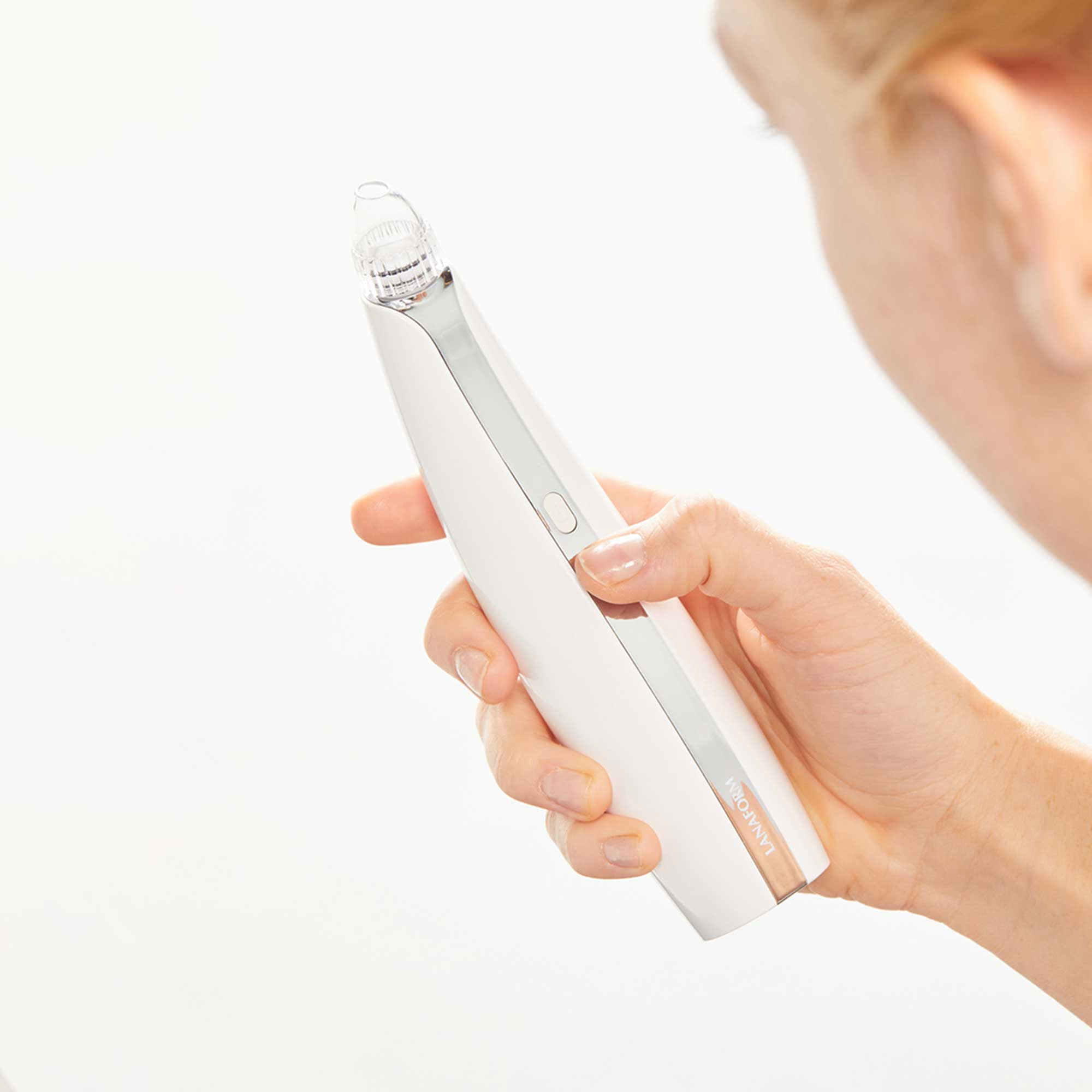 A woman's hand holds a white pore cleaner. The device is sleek and white, with a clear tip.