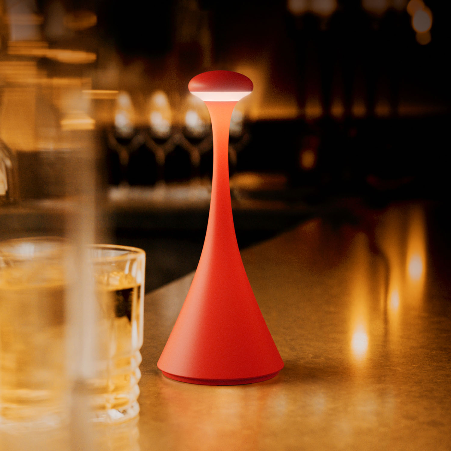 Rote Tischlampe auf einer Bar, mit verschwommenem Hintergrund aus Gläsern und Lichtern.
