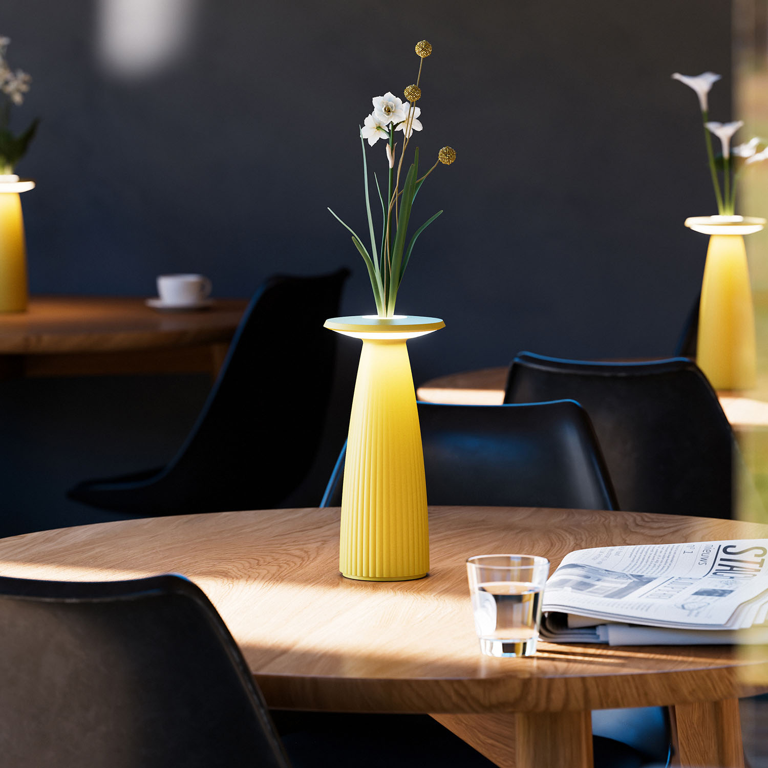 Eine gelbe Lampe mit Blumenarrangement auf einem Holztisch in einem Café.