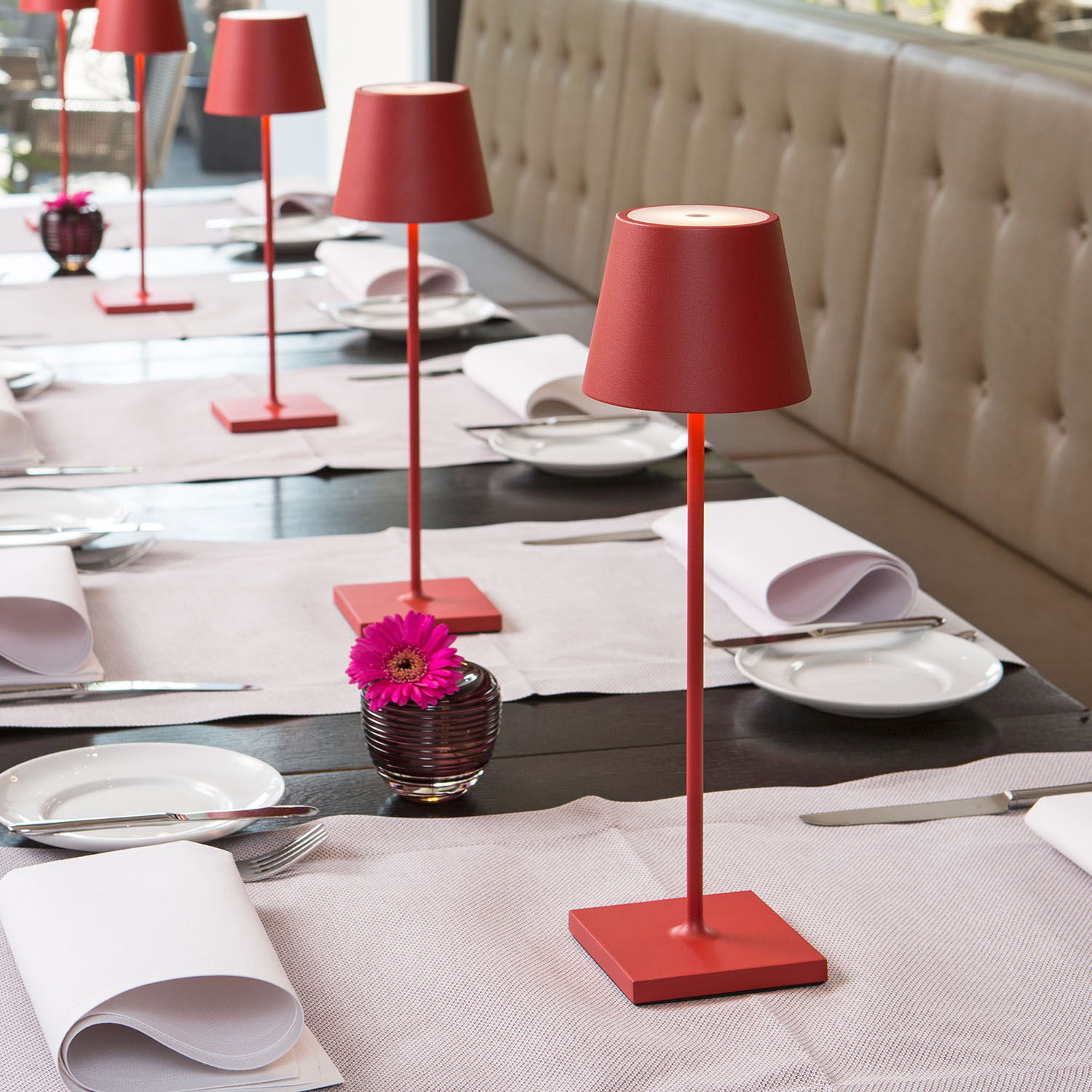 Rote Tischlampen auf einem Holztisch mit Gedecken und einer Blumenvase.