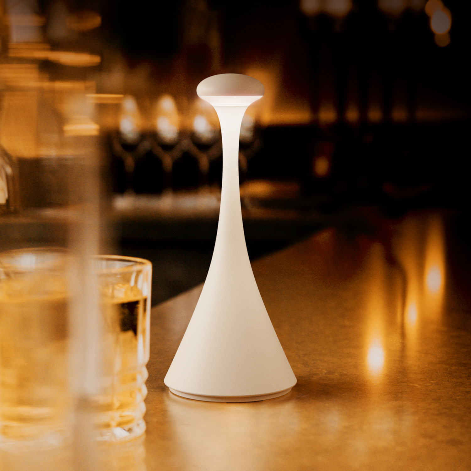 Eine weiße Lampe auf einem Tisch. Die Lampe ist kegelförmig und hat eine leuchtende Oberseite. Der Hintergrund ist unscharf.