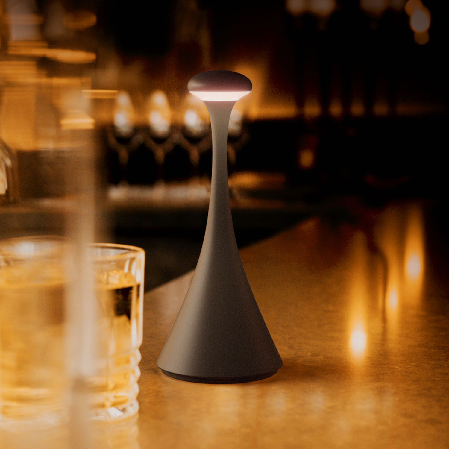 Eine schwarze Lampe steht auf einer Bar. Eine Hand berührt die Oberseite der Lampe, die leuchtet.