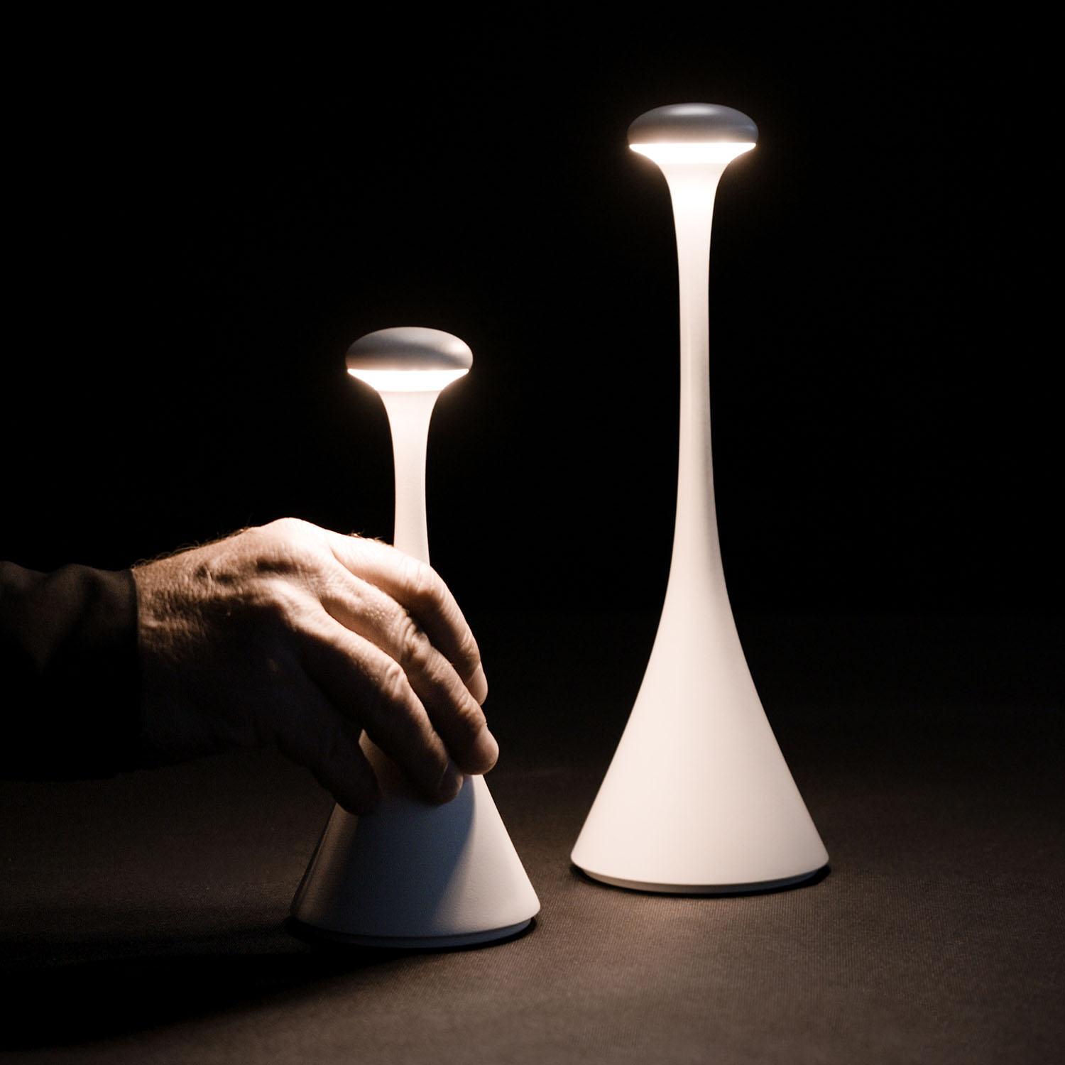 Zwei weiße, kegelförmige Lampen, eine Hand greift nach einer in dunkler Umgebung.