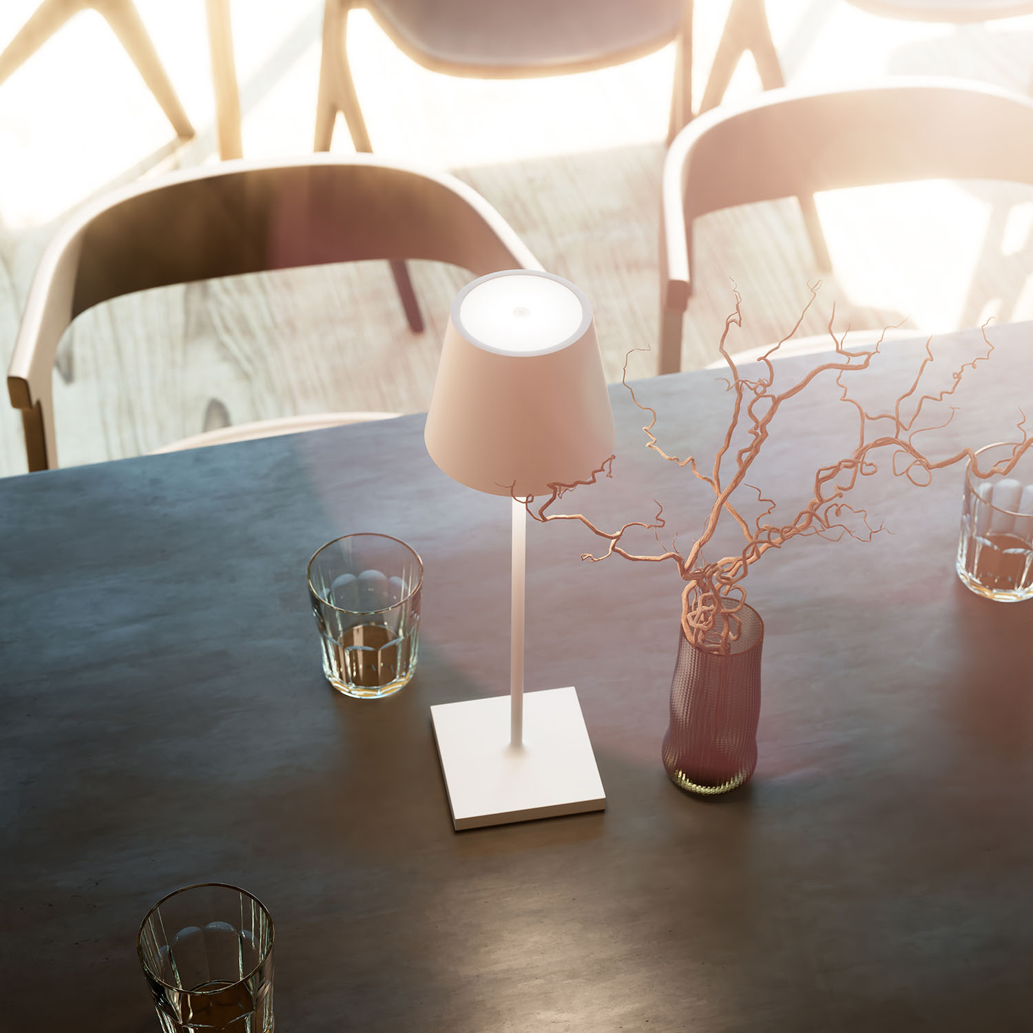 Ein Tisch mit Lampe, Gläsern und Vase mit Zweigen, was eine warme, einladende Atmosphäre schafft.