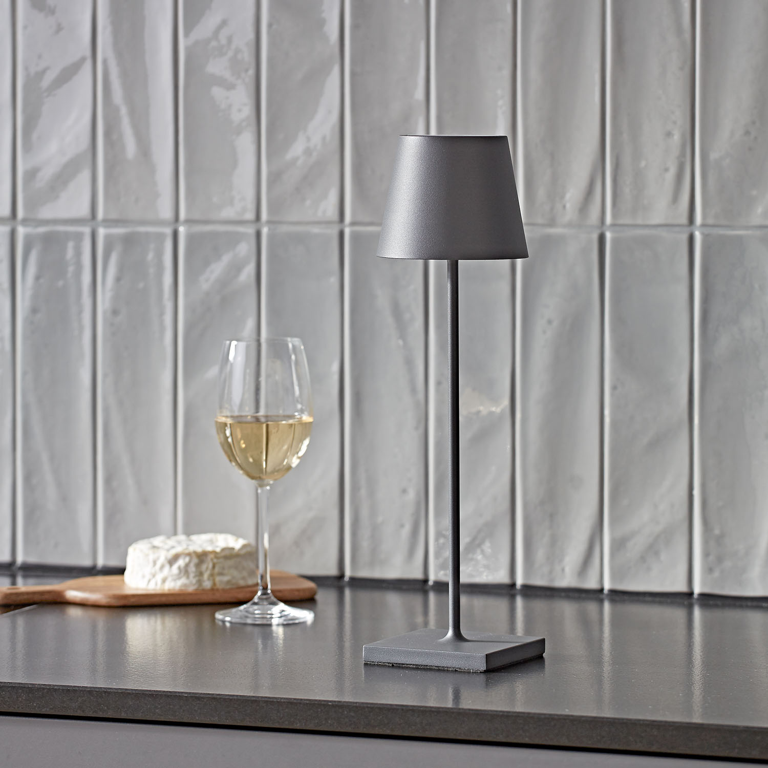 Tischlampe, Glas Weißwein und Käse auf Holzbrett auf einer Theke.