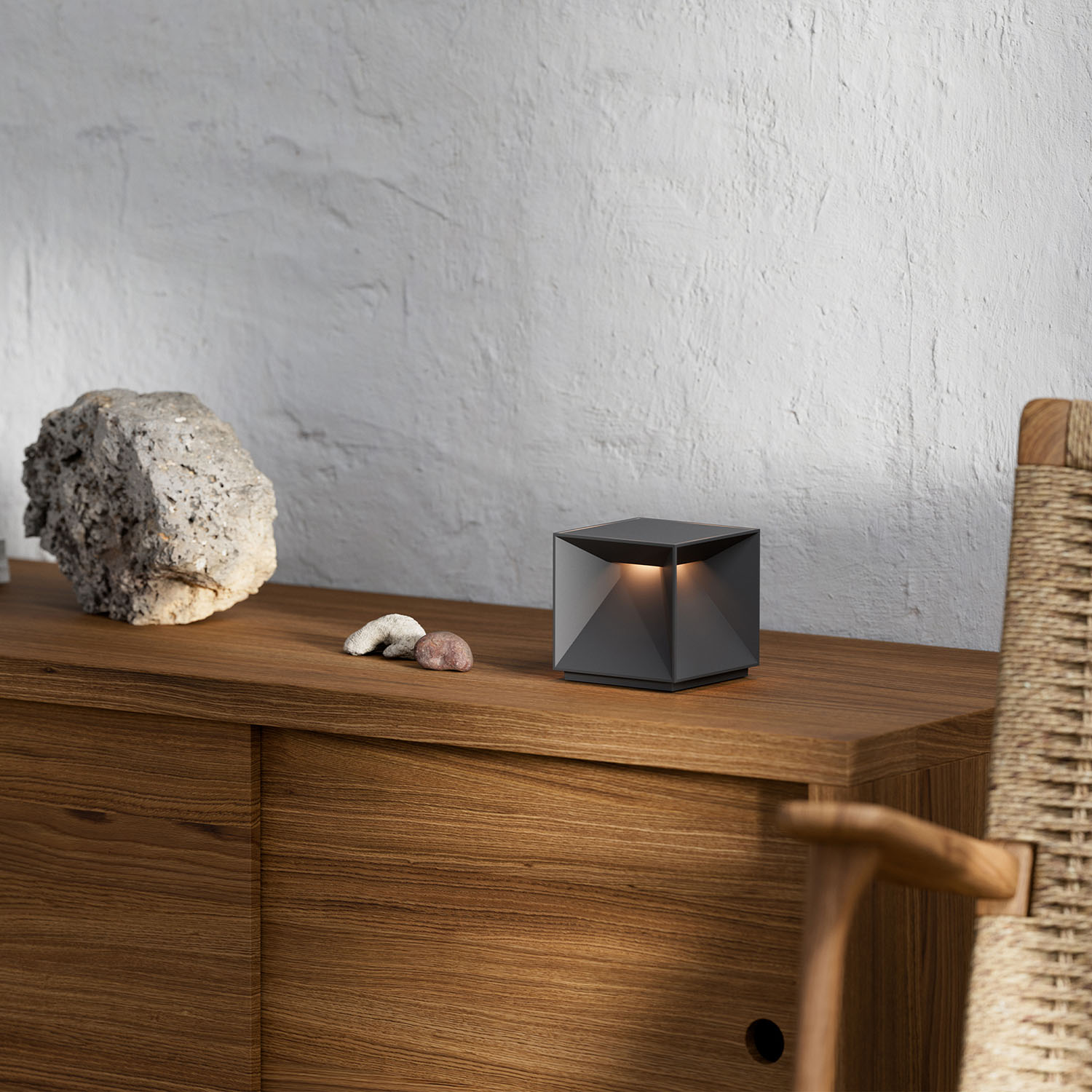 Eine moderne schwarze, würfelförmige Lampe auf Holz, mit Stein und Stuhl.