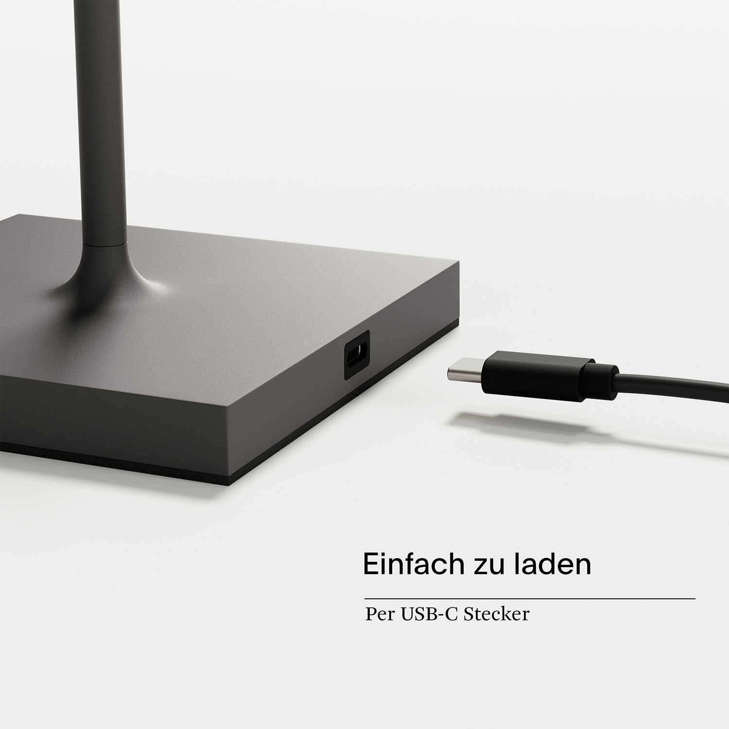 Ein grauer, quadratischer Sockel mit einem schwarzen Ladeanschluss. Ein schwarzes USB-C-Kabel ist eingesteckt.