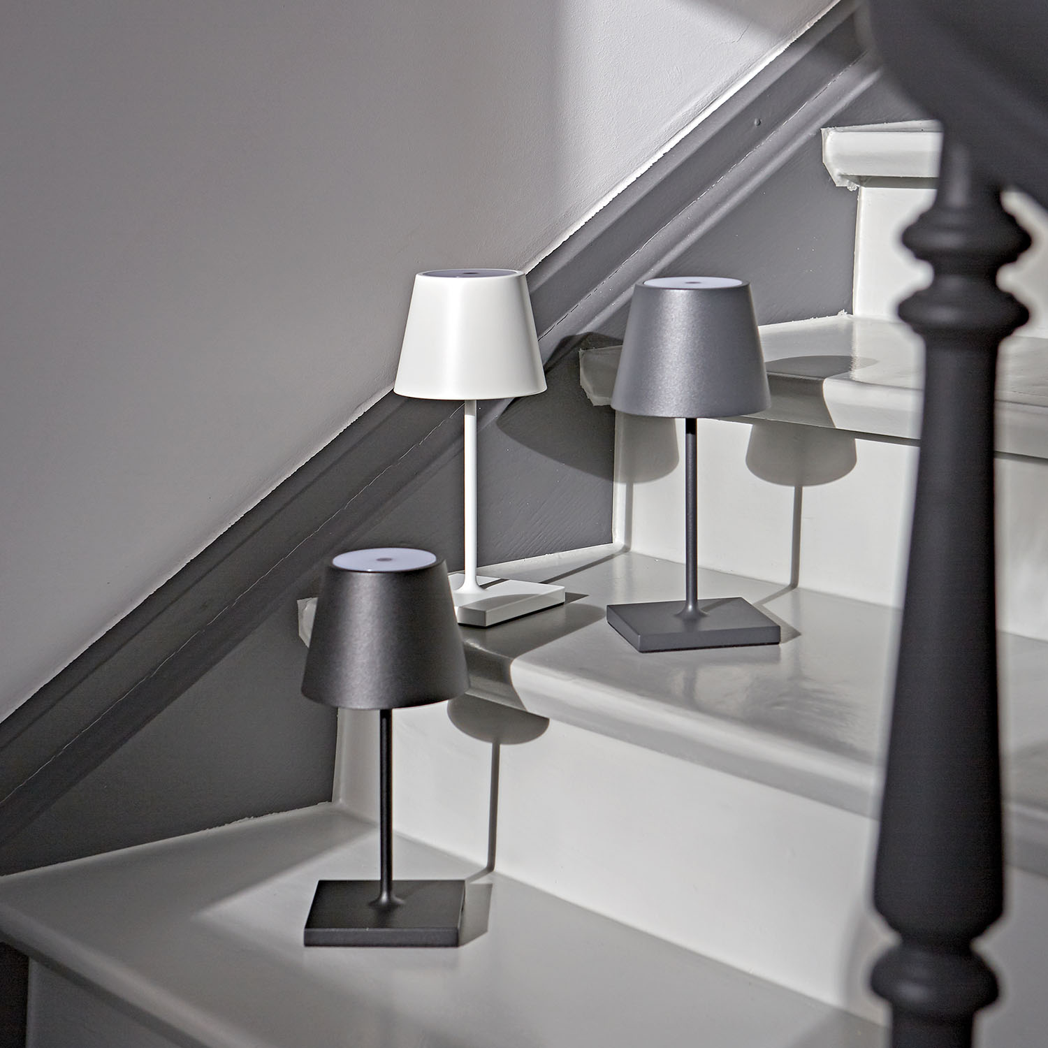 Drei Lampen auf einer Treppe. Eine weiße, eine graue und eine schwarze.