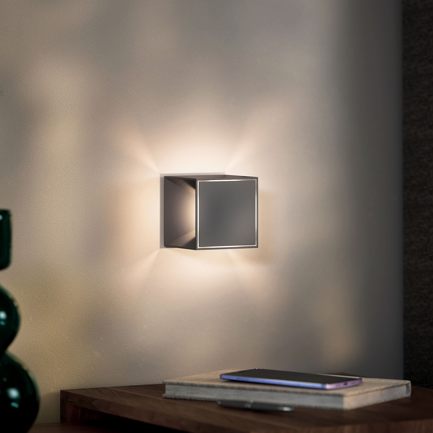 Eine quadratische schwarze Lampe, die an einer Wand montiert ist, mit nach unten scheinendem Licht.