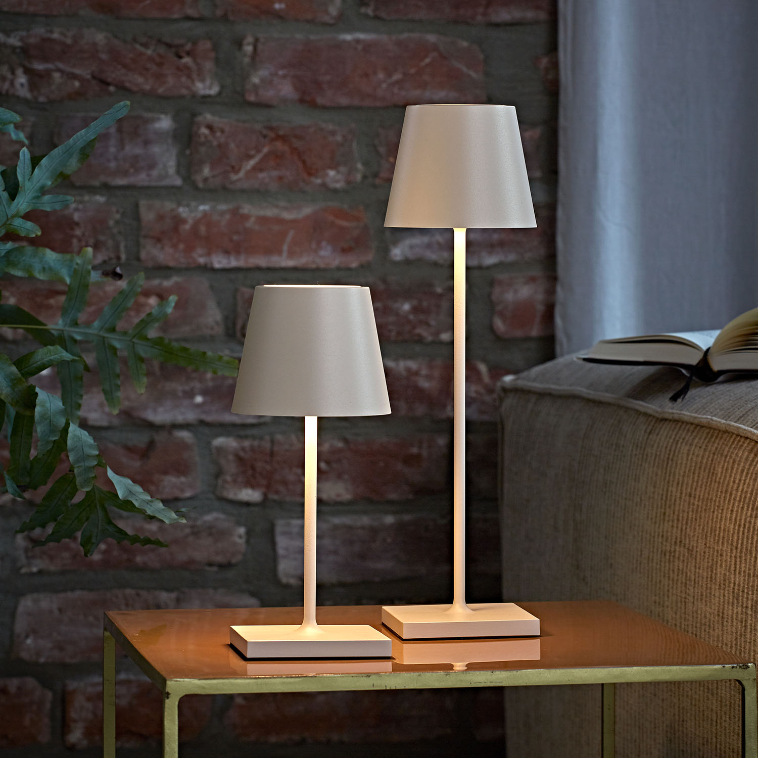 Zwei beige Lampen auf einem Tisch, Ziegelmauer im Hintergrund.