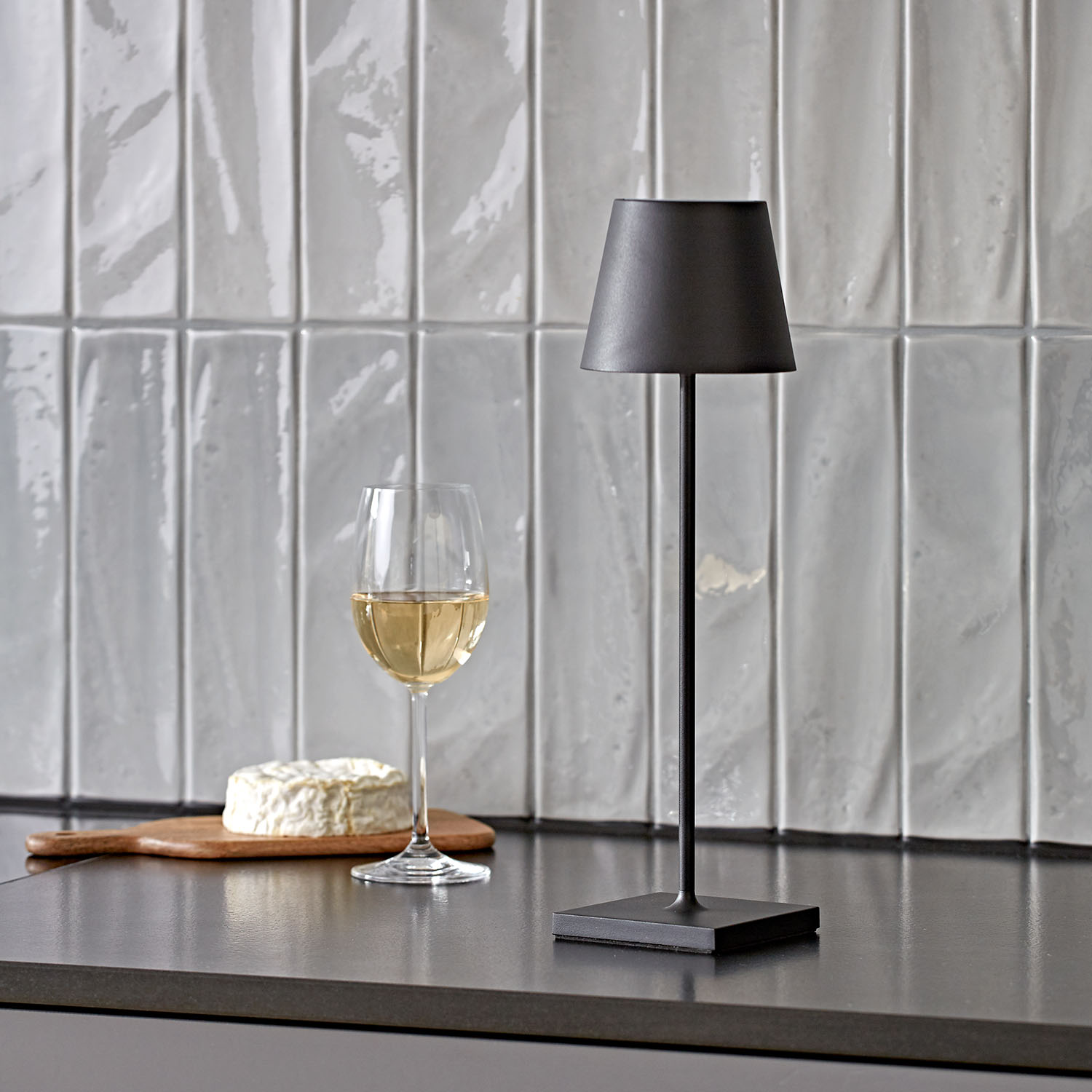 Lampada nera con bicchiere di vino e formaggio su una superficie grigia.