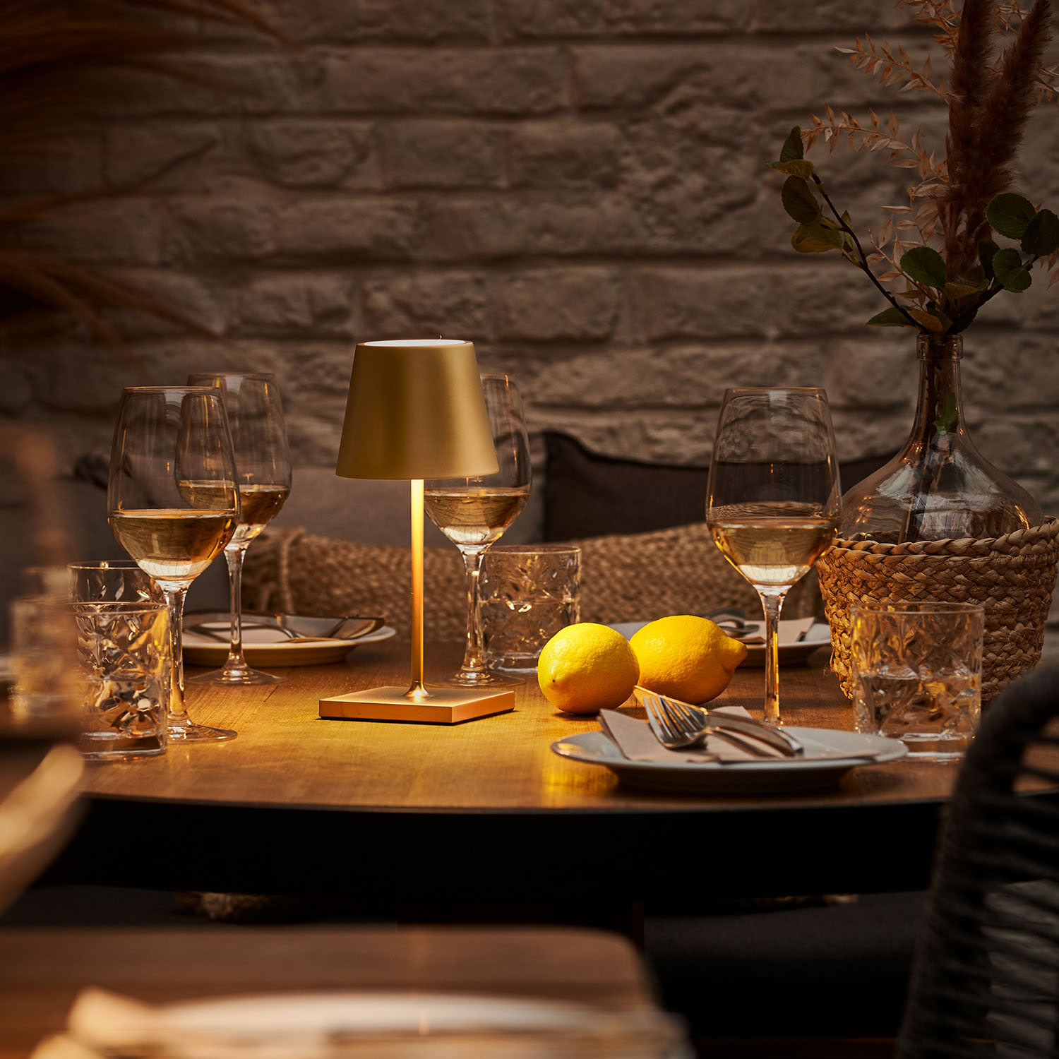 Ein Tisch mit Gläsern, Zitronen und einer Lampe. Die Szene ist beleuchtet. Hintergrund ist eine Ziegelmauer.