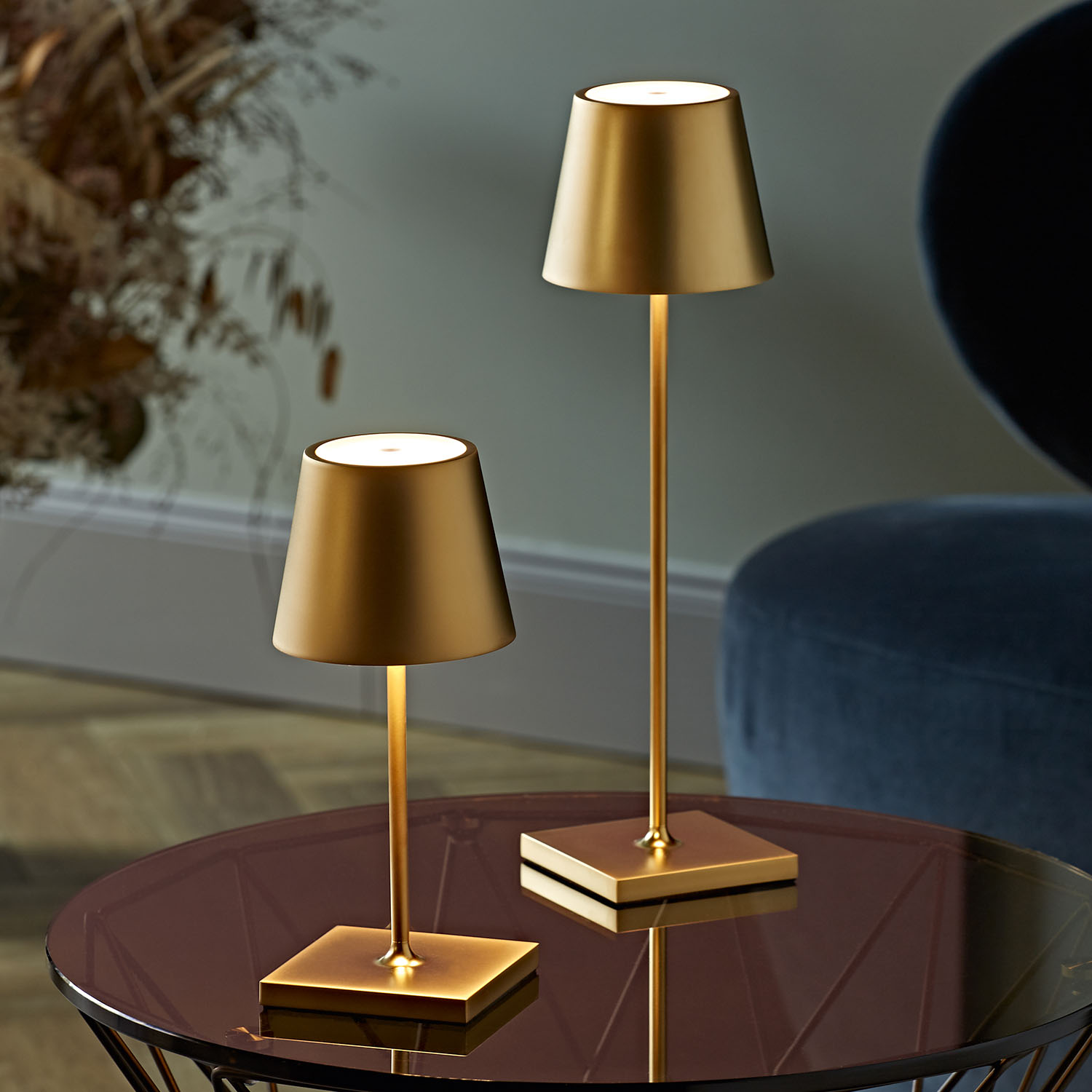 Zwei goldene Lampen mit Schirmen stehen auf einem Glastisch. Die Lampen leuchten.