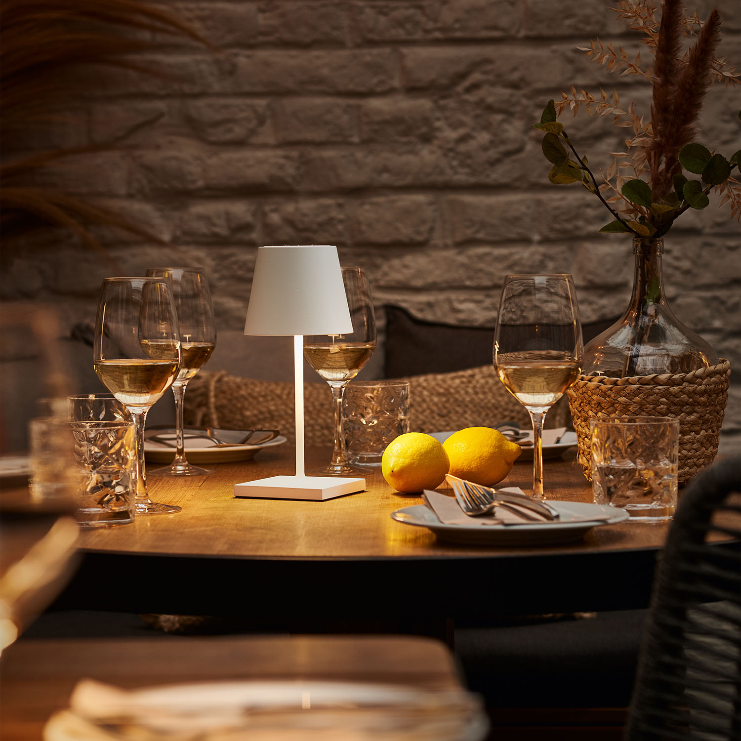 Ein Tisch mit Gläsern, Wein, Zitronen und einer weißen Lampe in einem schwach beleuchteten Raum.