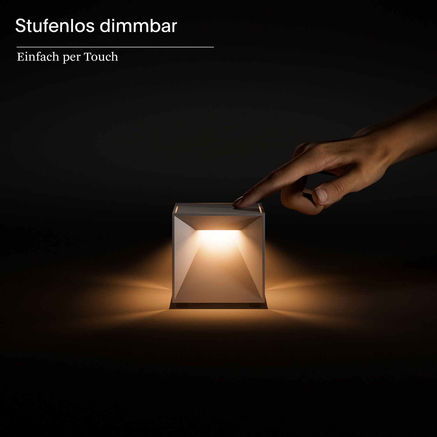 Eine Hand berührt eine Würfellampe und beleuchtet sie. Die Lampe steht auf dunkler Oberfläche, erzeugt warmes Leuchten.