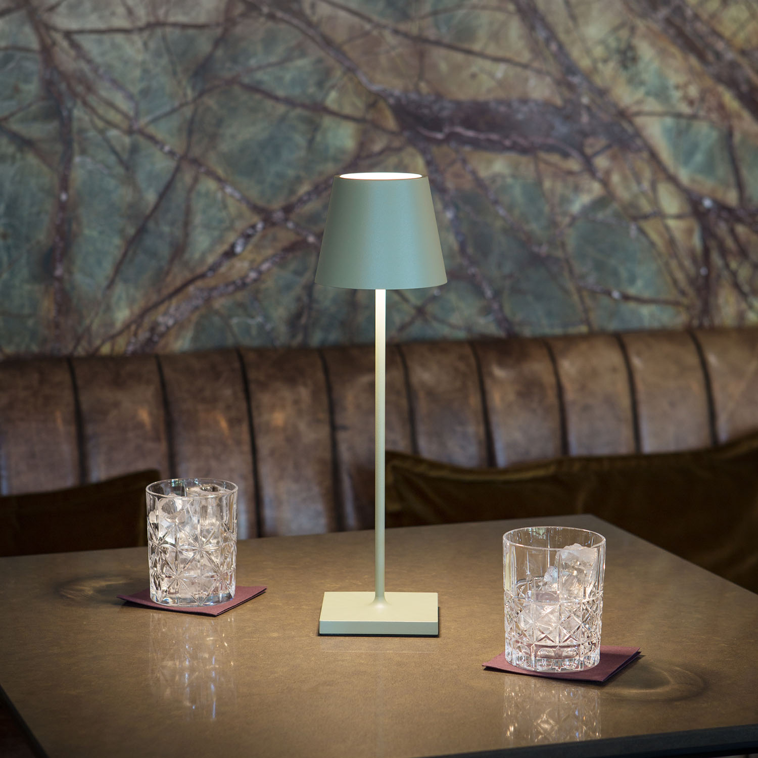 Grüne Lampe auf einem Tisch mit zwei Eisgläsern. Marmorartiger Hintergrund, dunkle Holzbar.