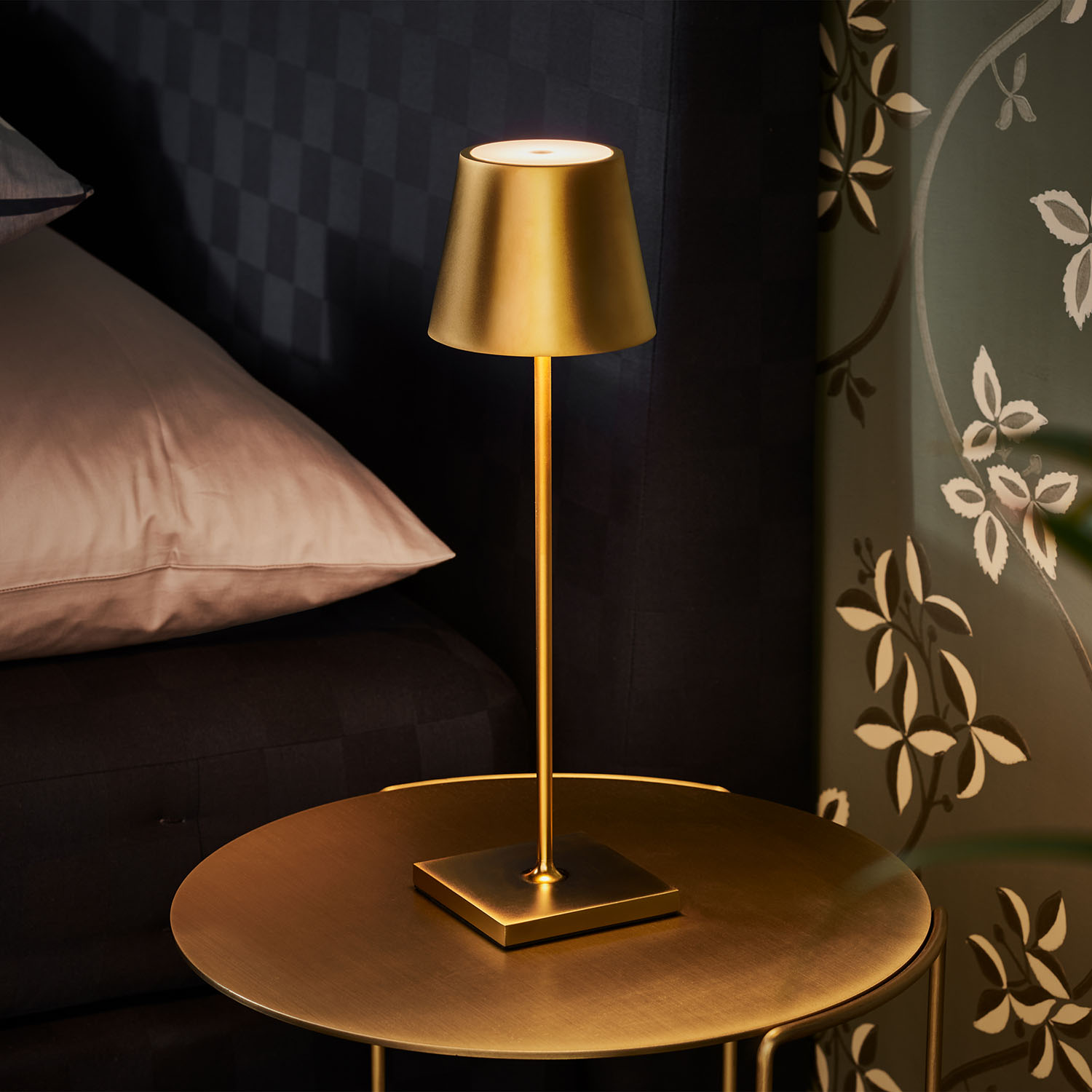 Eine goldene Lampe auf einem goldenen Tisch. Ein Bett und Tapete im Hintergrund.