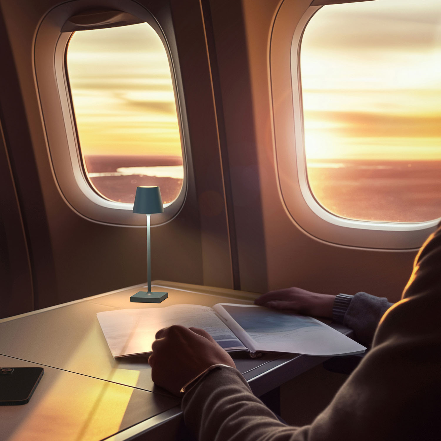 Eine Person im Flugzeug, die ein Buch mit einer kleinen Lampe auf dem Tisch betrachtet.