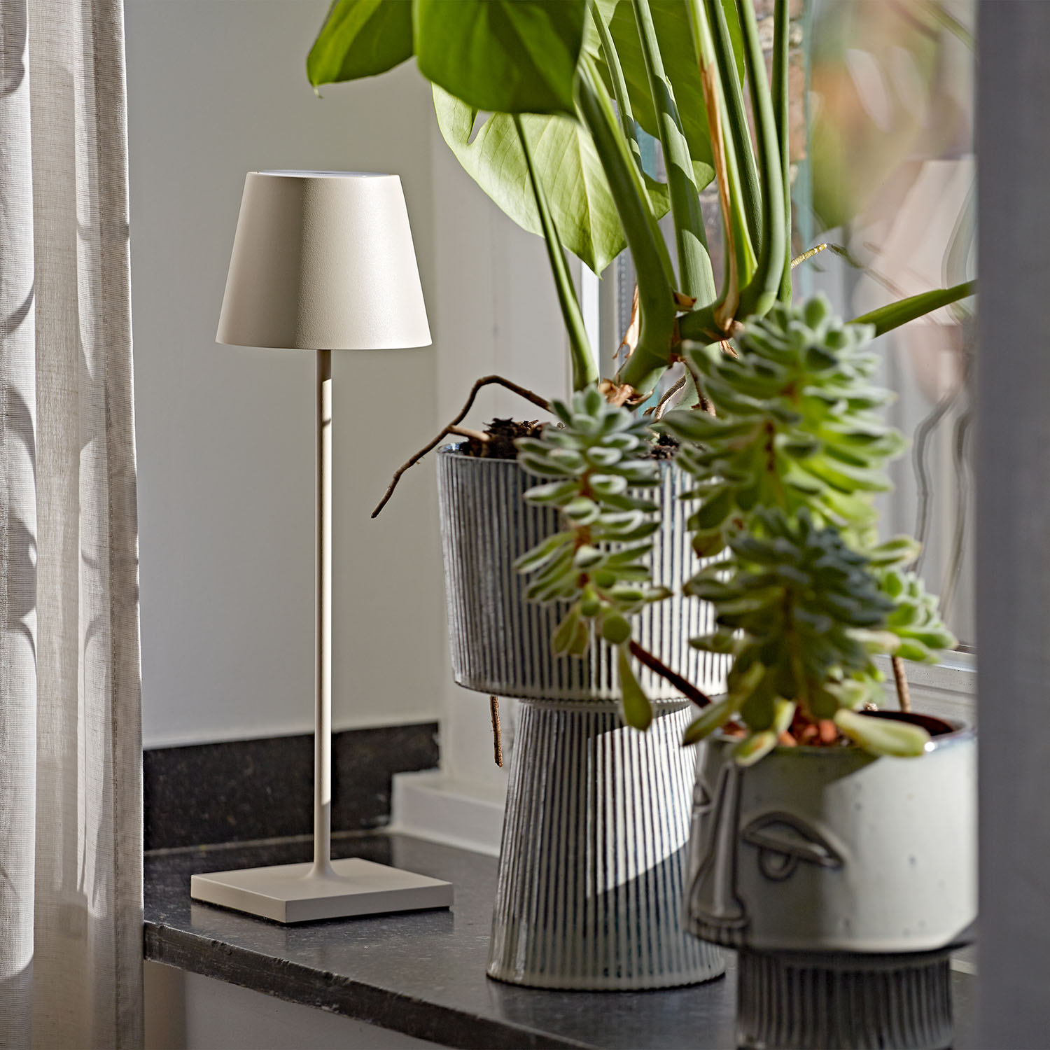 Lampe auf einem Ständer neben Pflanzen und einem Fenster mit Vorhang.