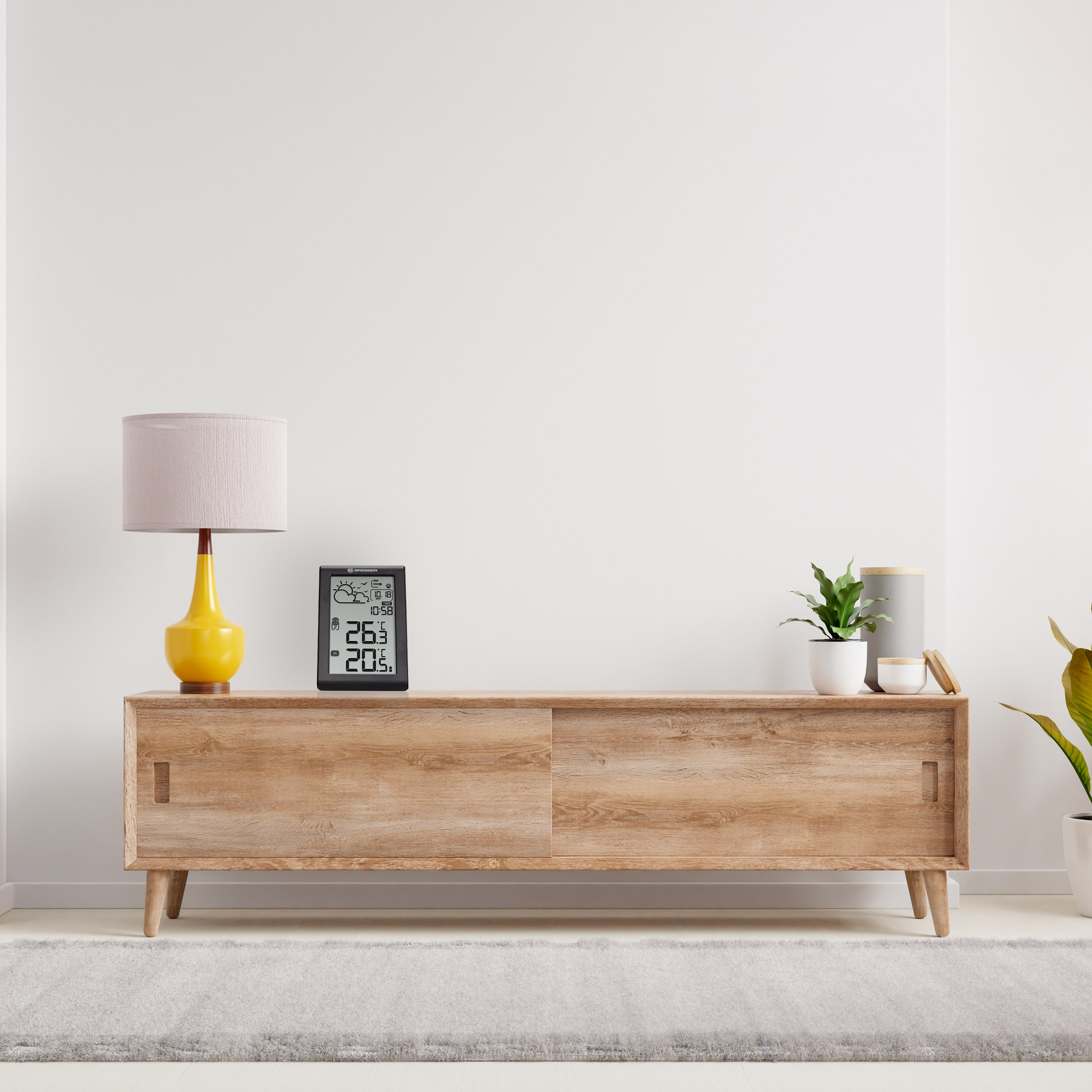 Ein Holzschrank mit Lampe, Pflanze und Digitaluhr oben drauf.