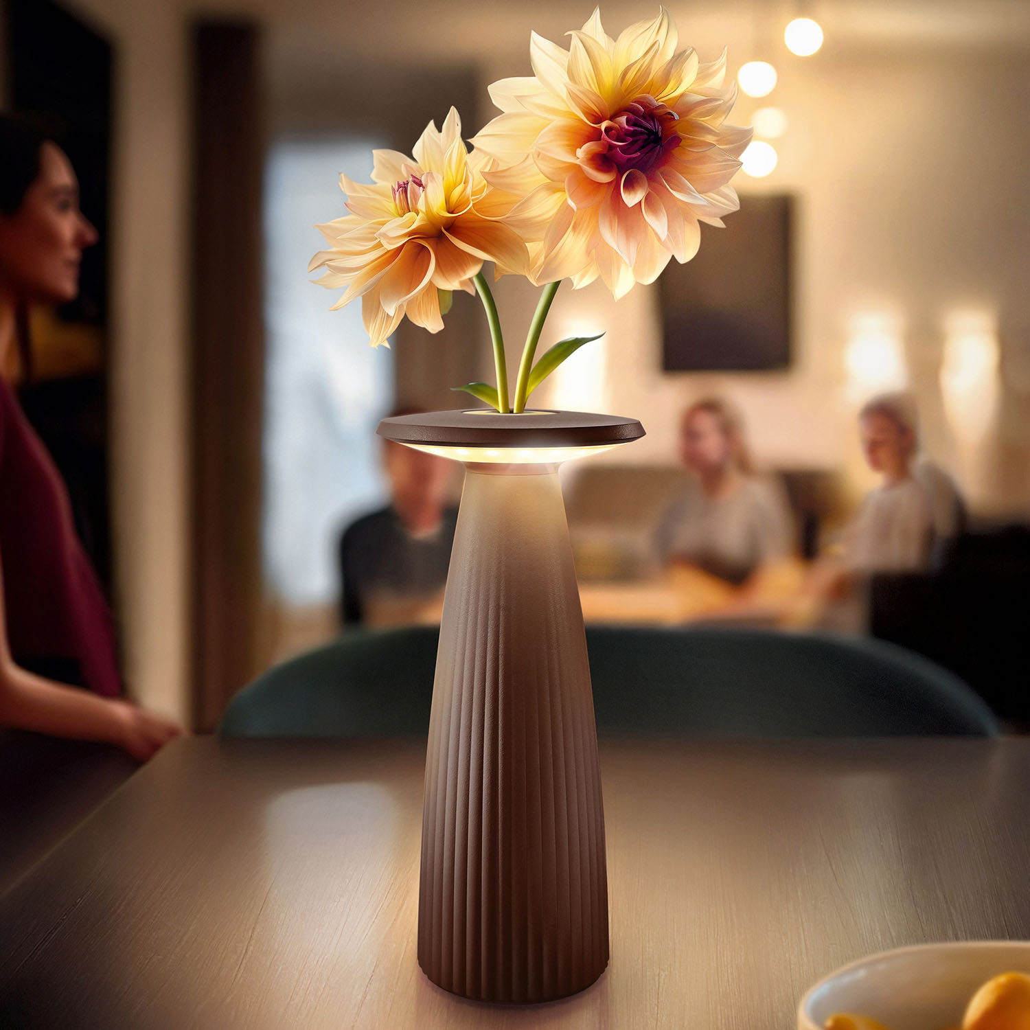 Zwei Blumen in einer Vase mit Lampe auf einem Tisch, Menschen im Hintergrund, erzeugt eine warme Atmosphäre.