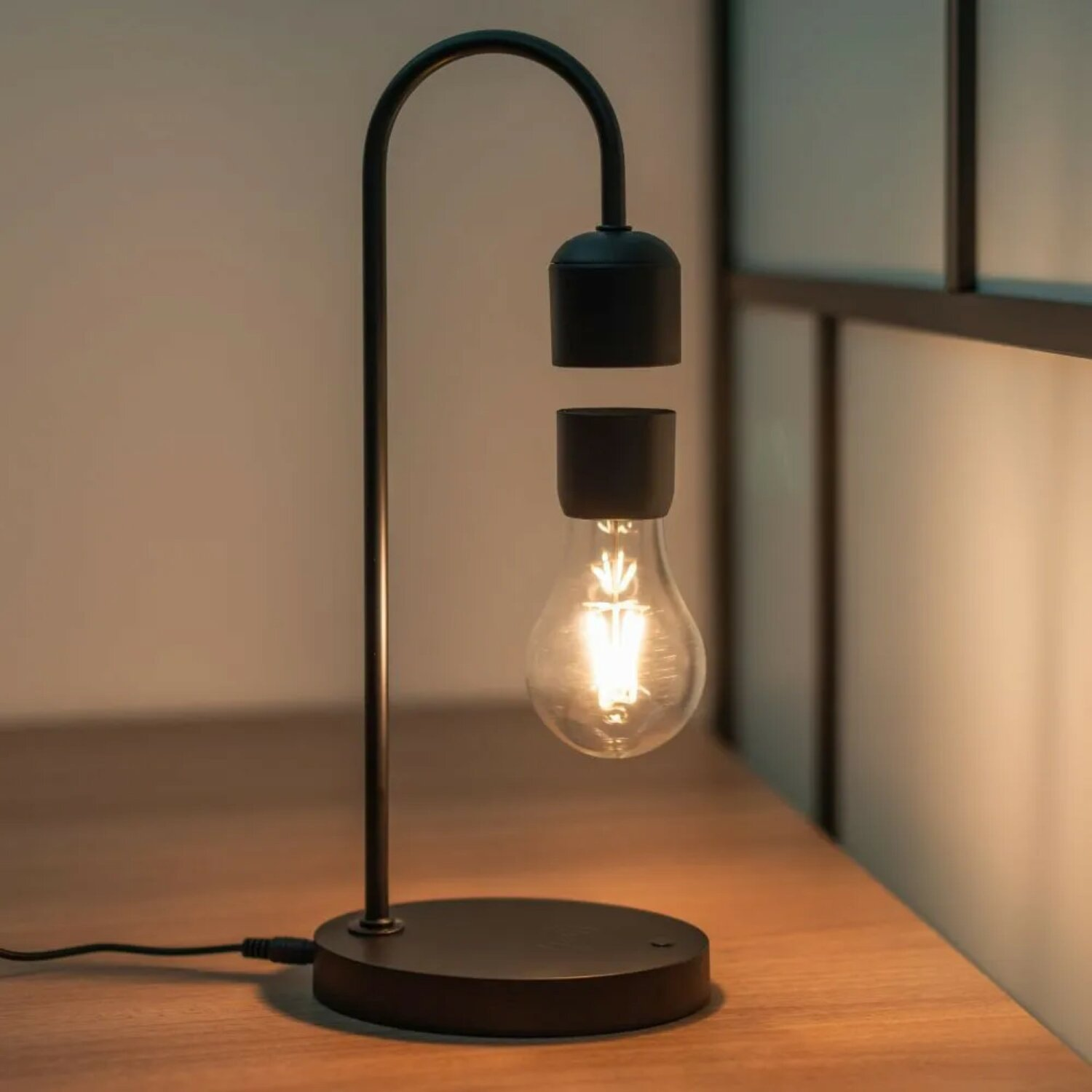 Schwebende Glühbirnenlampe, schwarzer Sockel und Stütze, mit einer leuchtenden Glühbirne.